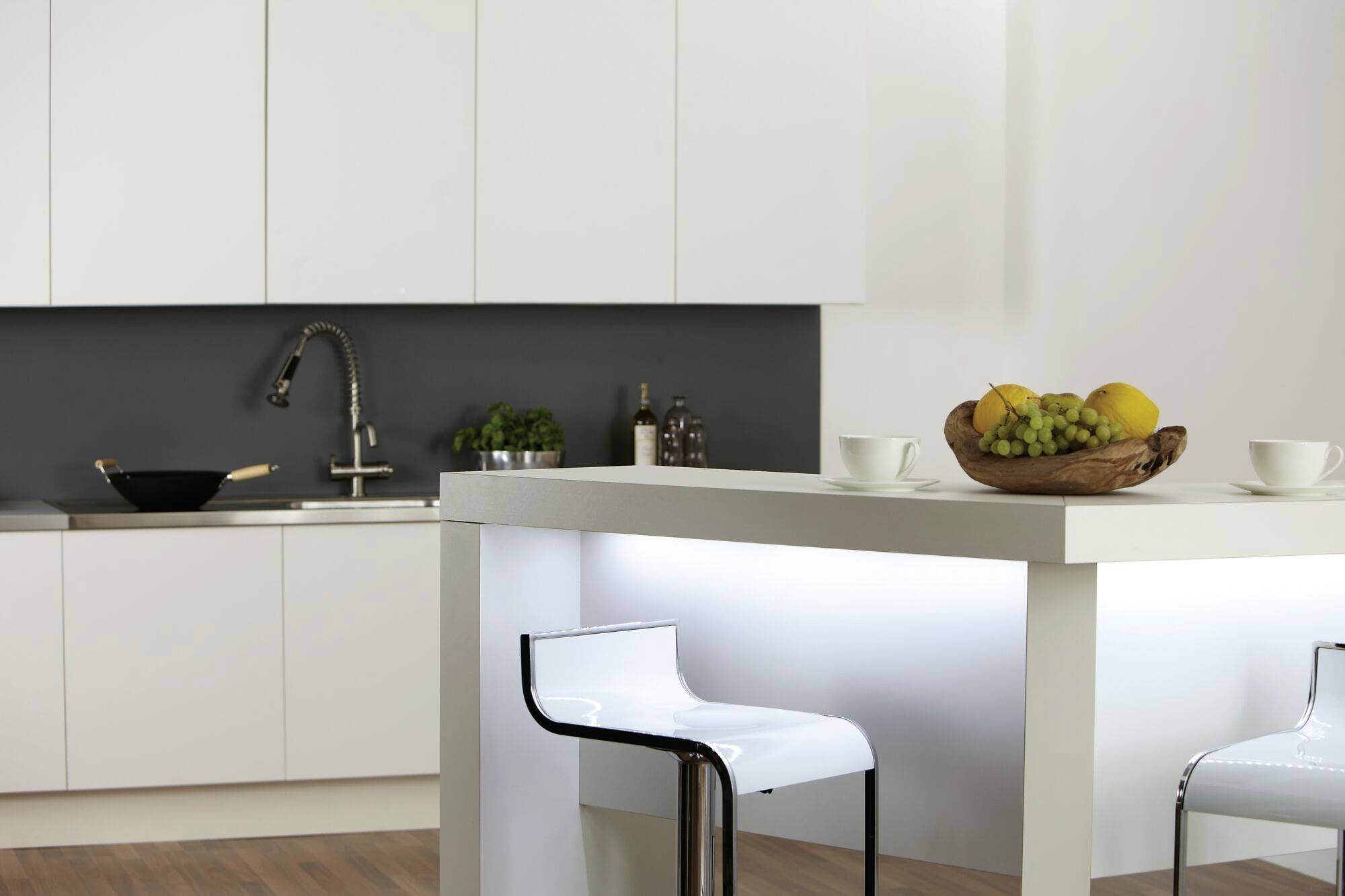 Modern kitchen with white cupboards, a sink and a fruit basket with lemons and grapes on the table.