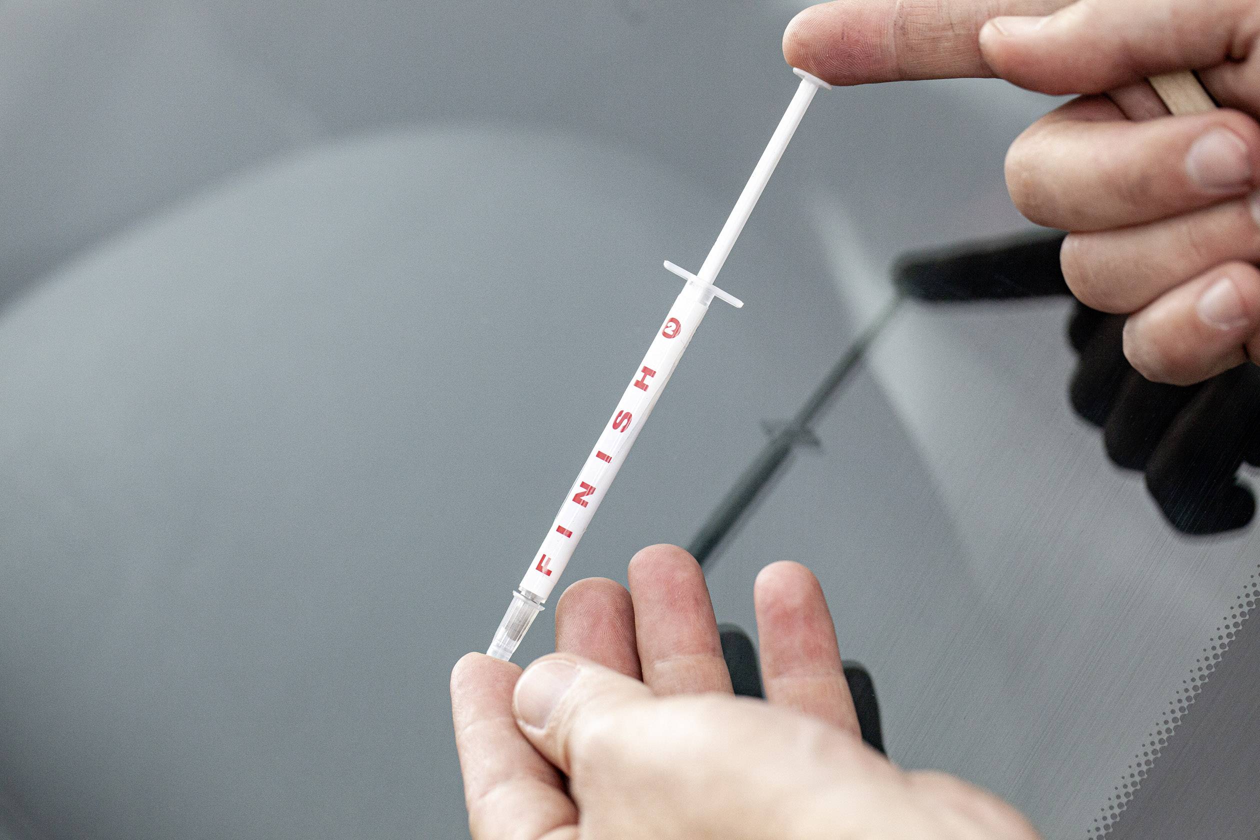 A person is holding a needle with the inscription 'FINISH' near a smashed car window.