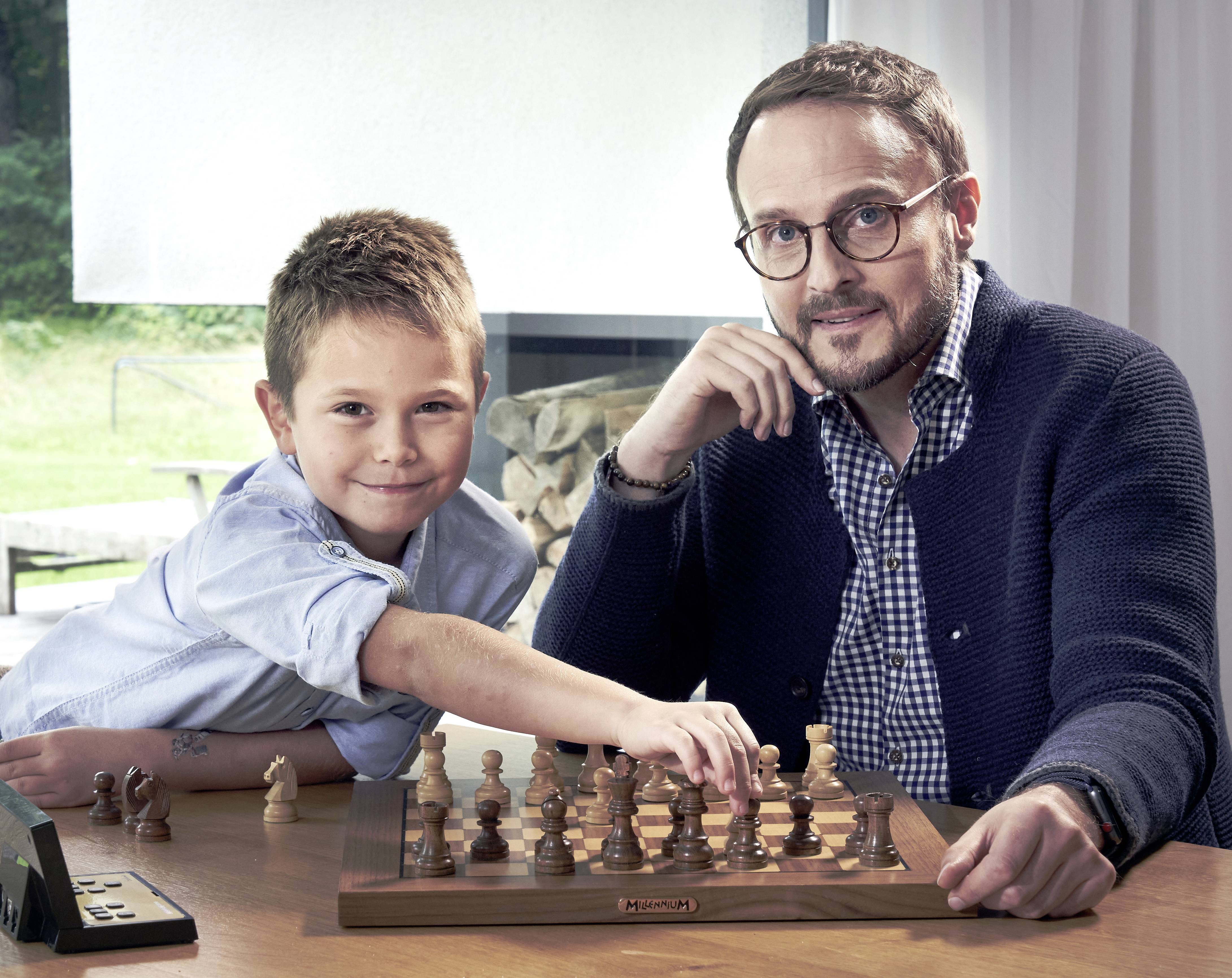 A boy and a man are playing chess at a table in a modern, bright room. The boy smiles as he makes a move.