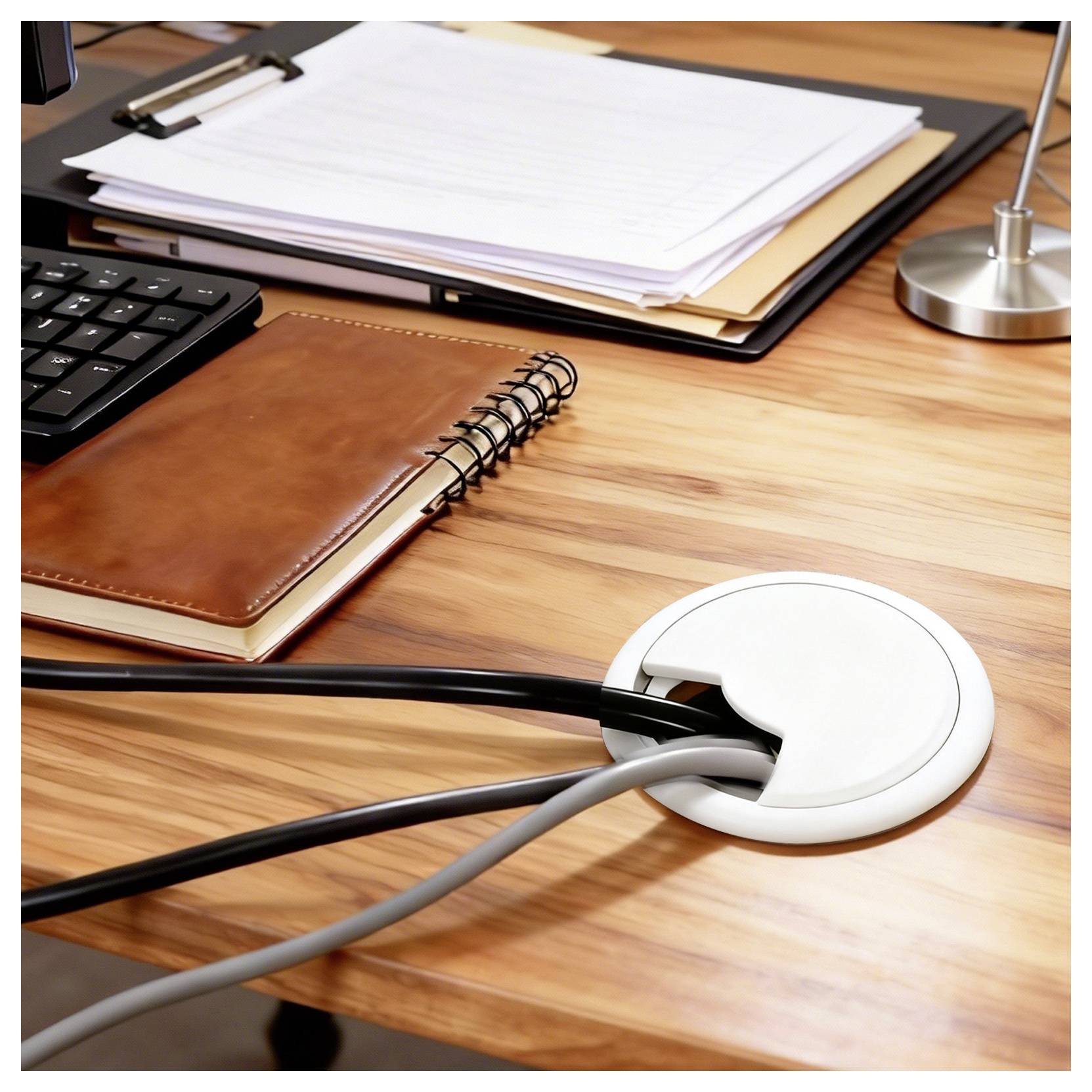 A wooden desk with a black keyboard, brown notebook, and documents. Cables emerge from a white cable management grommet.
