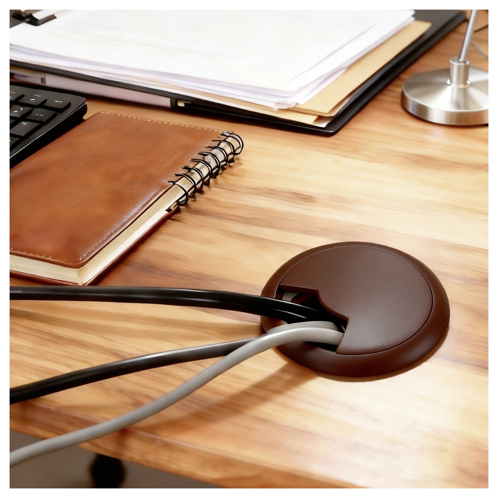 A tidy desk with a notebook, keyboard, and a cable organizer directing wires through a hole, creating an organized workspace.