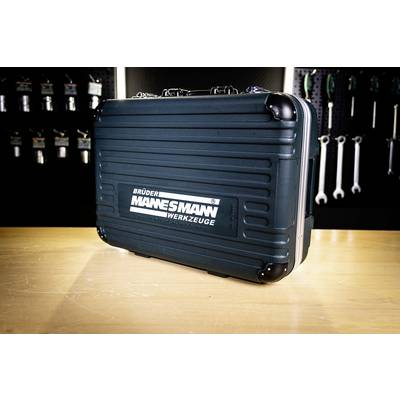 A black tool case with 'Brüder Mannesmann Werkzeuge' label on a wooden table. Background features hanging tools on a wall.