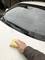 A person is cleaning the bonnet of a white car with a yellow sponge. The car is parked in a courtyard.