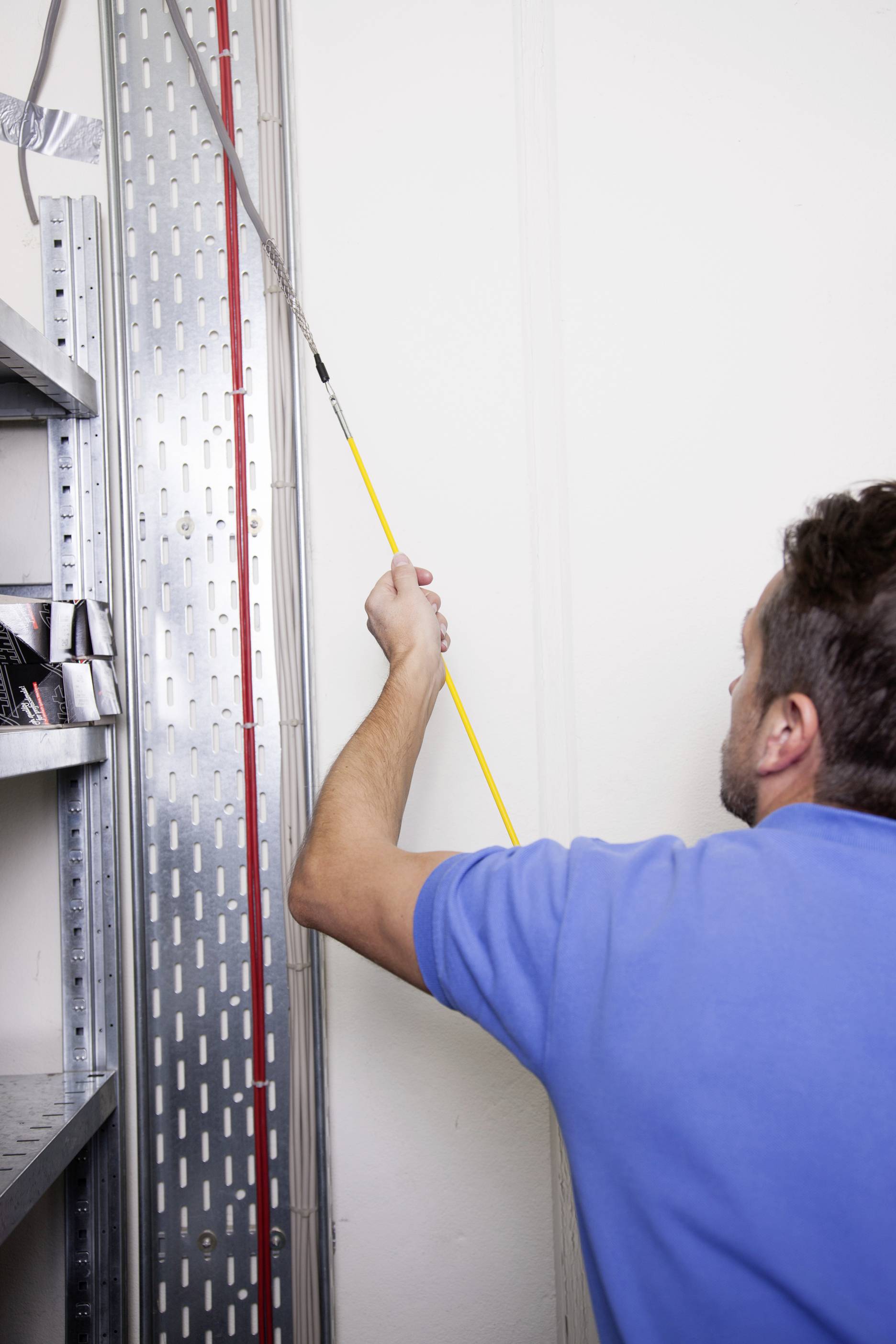 Man in blue shirt checking wiring on a wall in the server room.