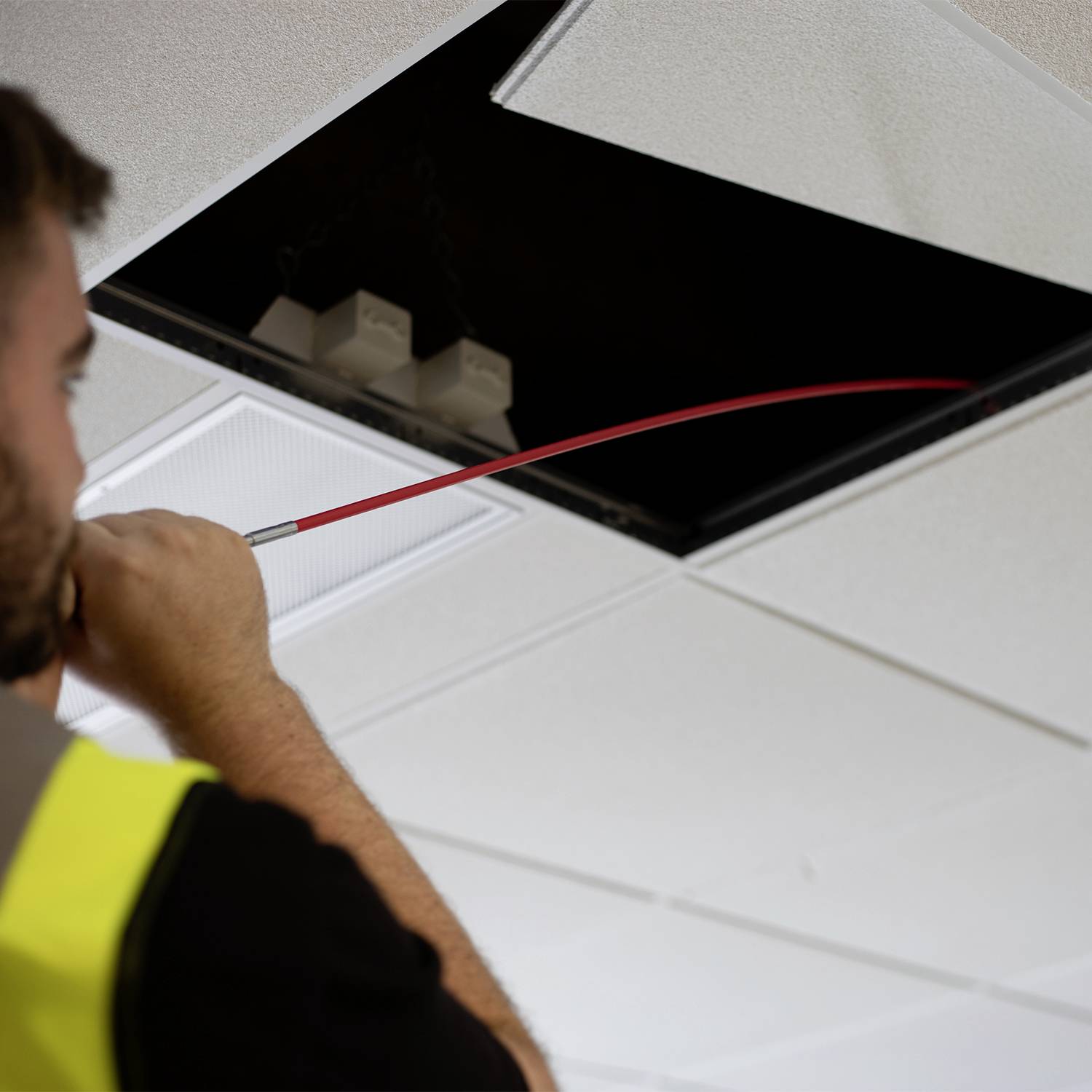 A person is installing a red cable in a ceiling opening, presumably for electrical or technical work.