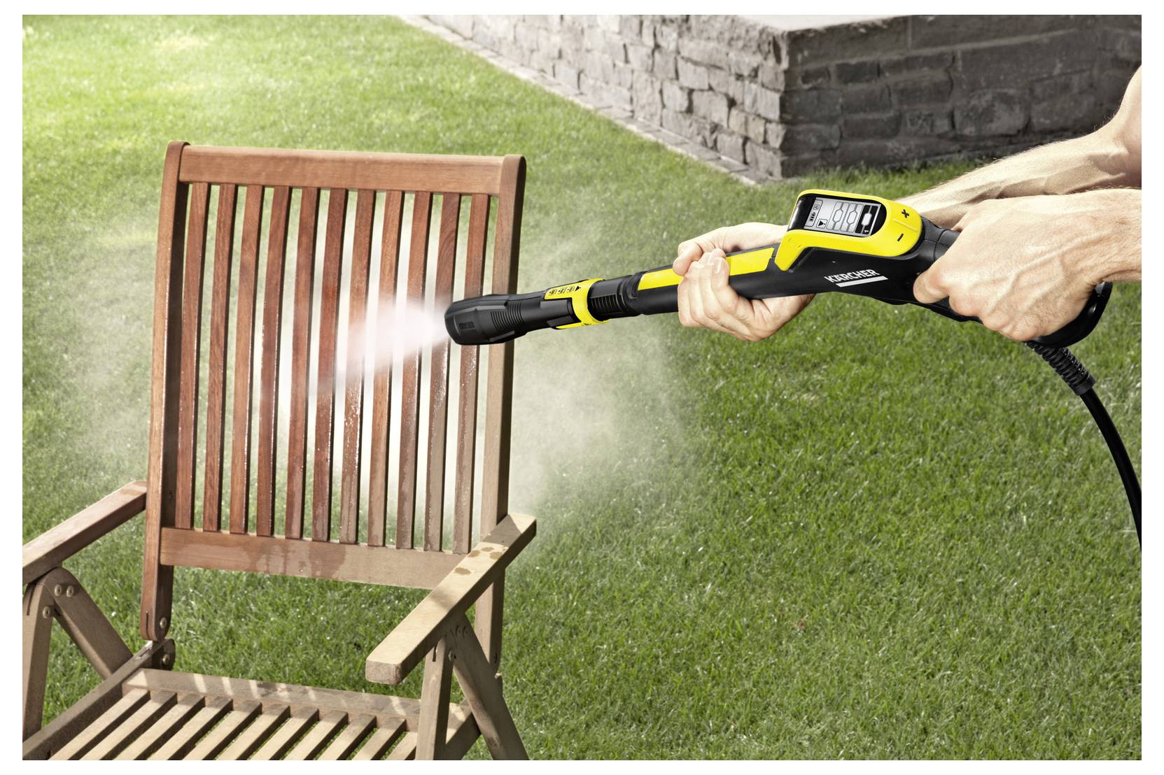 A person is using a yellow pressure washer to clean a wooden chair outdoors on a lawn, with water visibly spraying on the chair.