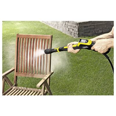 A person is using a yellow pressure washer to clean a wooden chair outdoors on a lawn, with water visibly spraying on the chair.