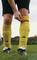 A player wearing yellow socks tightens a red sock tape over their ankle on a football pitch.