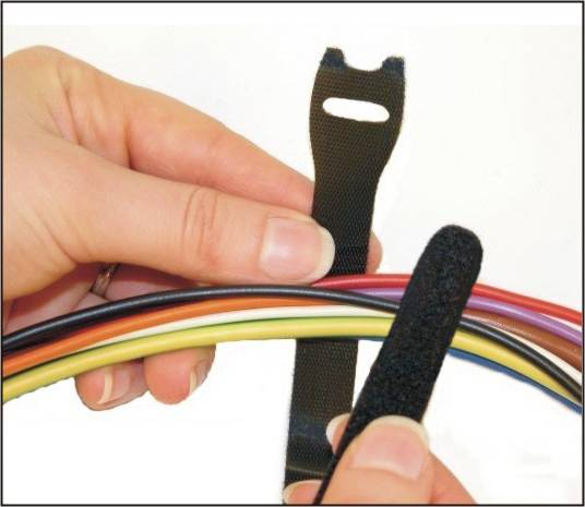 A person is binding colourful cables together with a black hook-and-loop fastener.