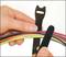A hand holds several coloured cables together, while the other hand points to a hook-and-loop fastener for securing the cables.