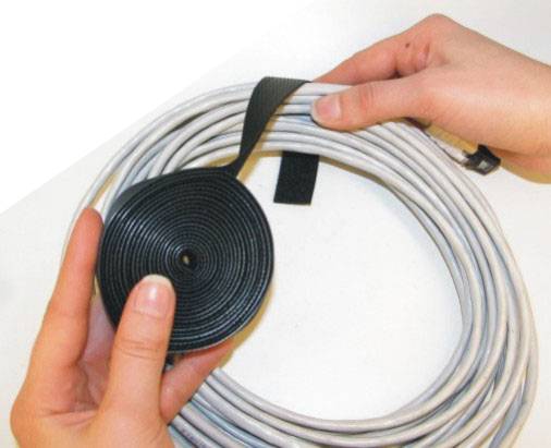 A person is holding copper cables bound together with hook-and-loop fastener. Hands are demonstrating the application of the binding tape.