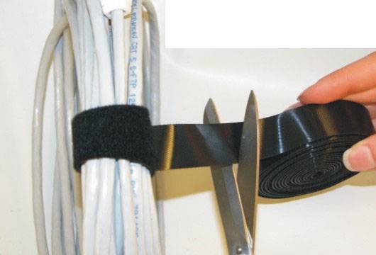 A hand cuts through a hook-and-loop fastener (Velcro) holding the cable with a pair of scissors.