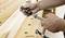 A person is mounting a woodworking bench clamp on a wooden workbench to securely hold workpieces in place.