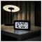 A digital alarm clock displays '12:00 AM' on a bedside table next to a lit modern lamp, suggesting nighttime or early morning.