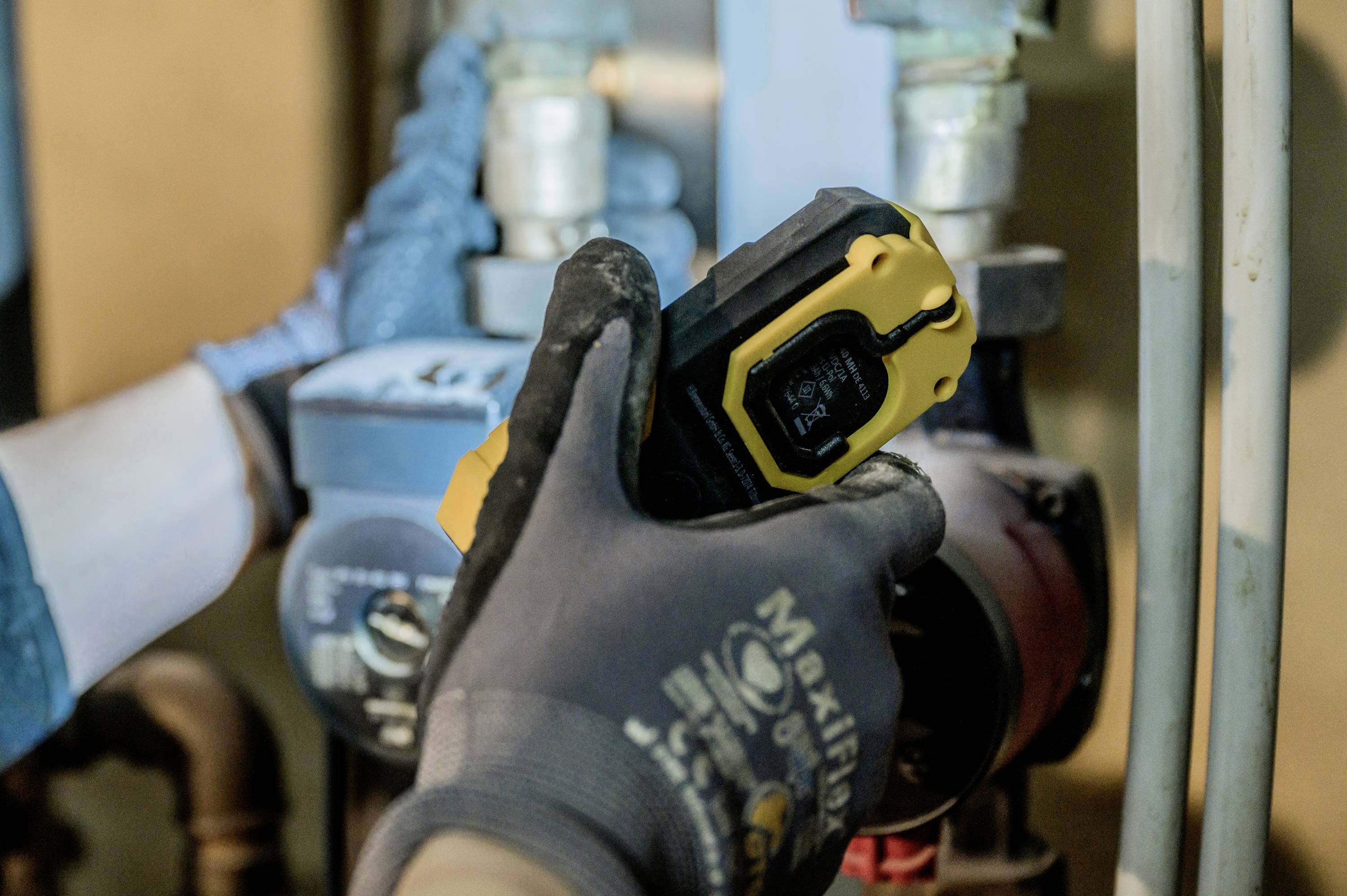 A person wearing gloves is holding an infrared thermometer against a pipeline valve, apparently to measure the temperature.