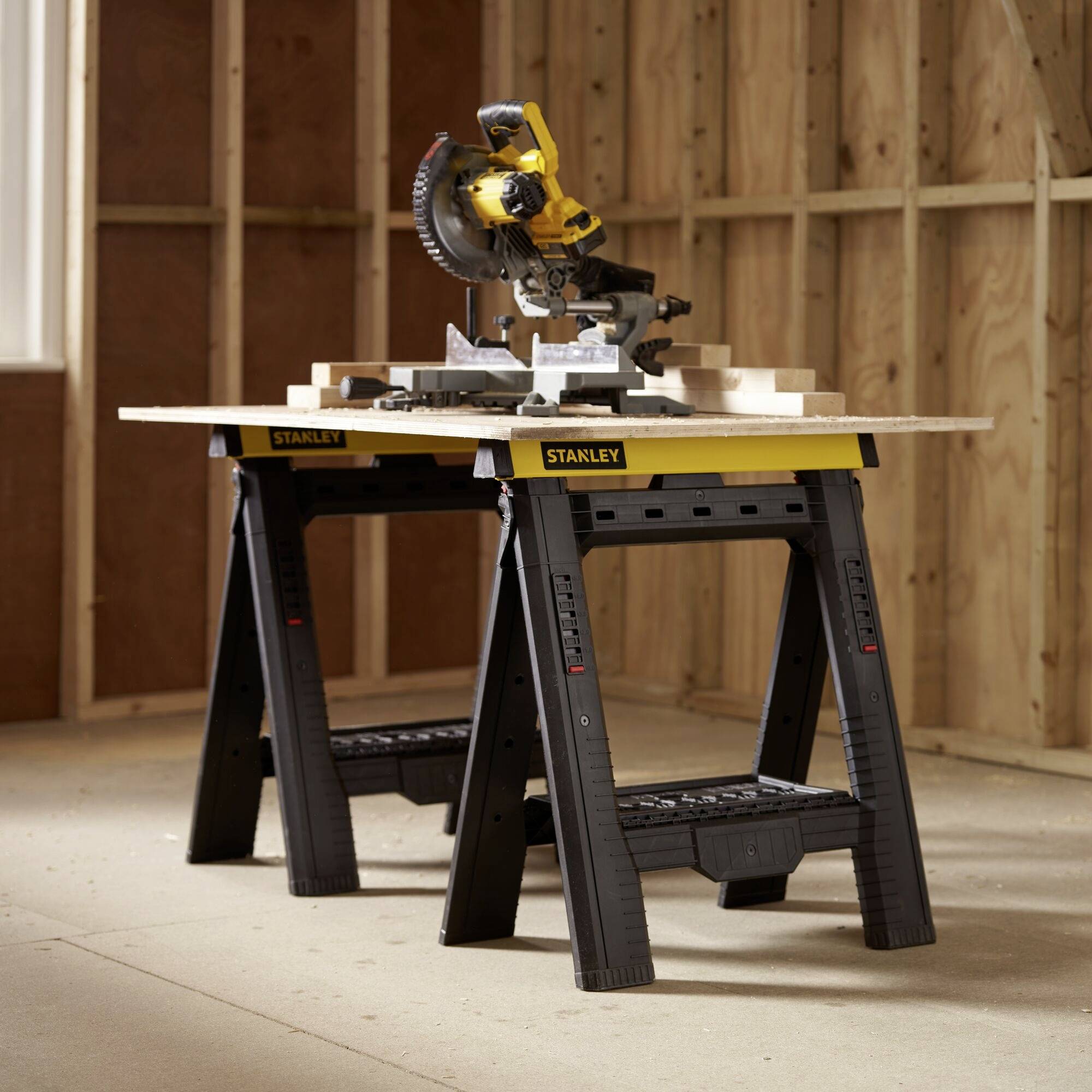 A mitre saw on a Stanley workbench in an unfinished woodworking workshop. It is ready to cut pieces of wood.
