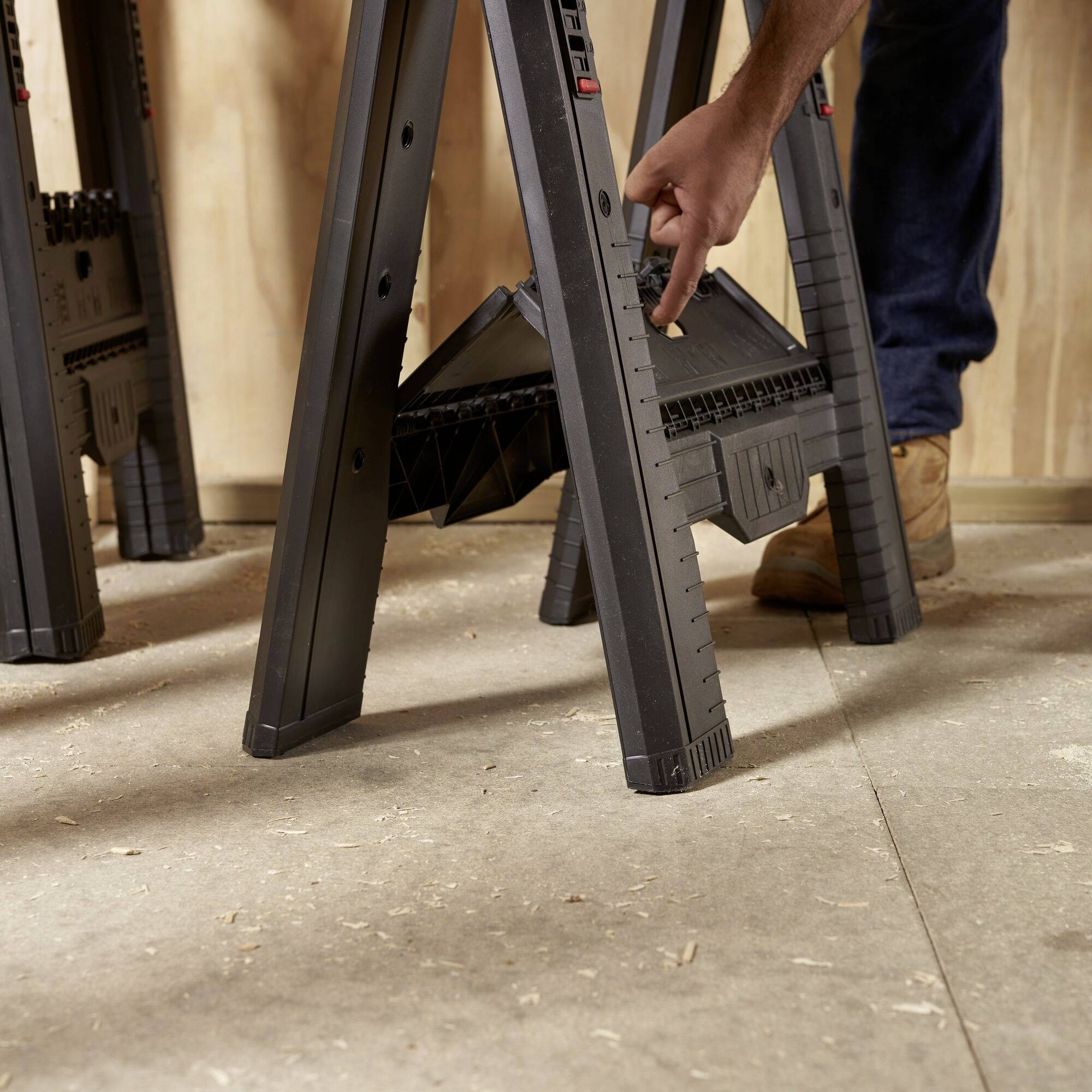 A person is mounting or adjusting a black saw horse device on a wooden floor.