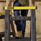A person wearing jeans and boots is standing on a yellow Stanley tool stand in a workshop environment.