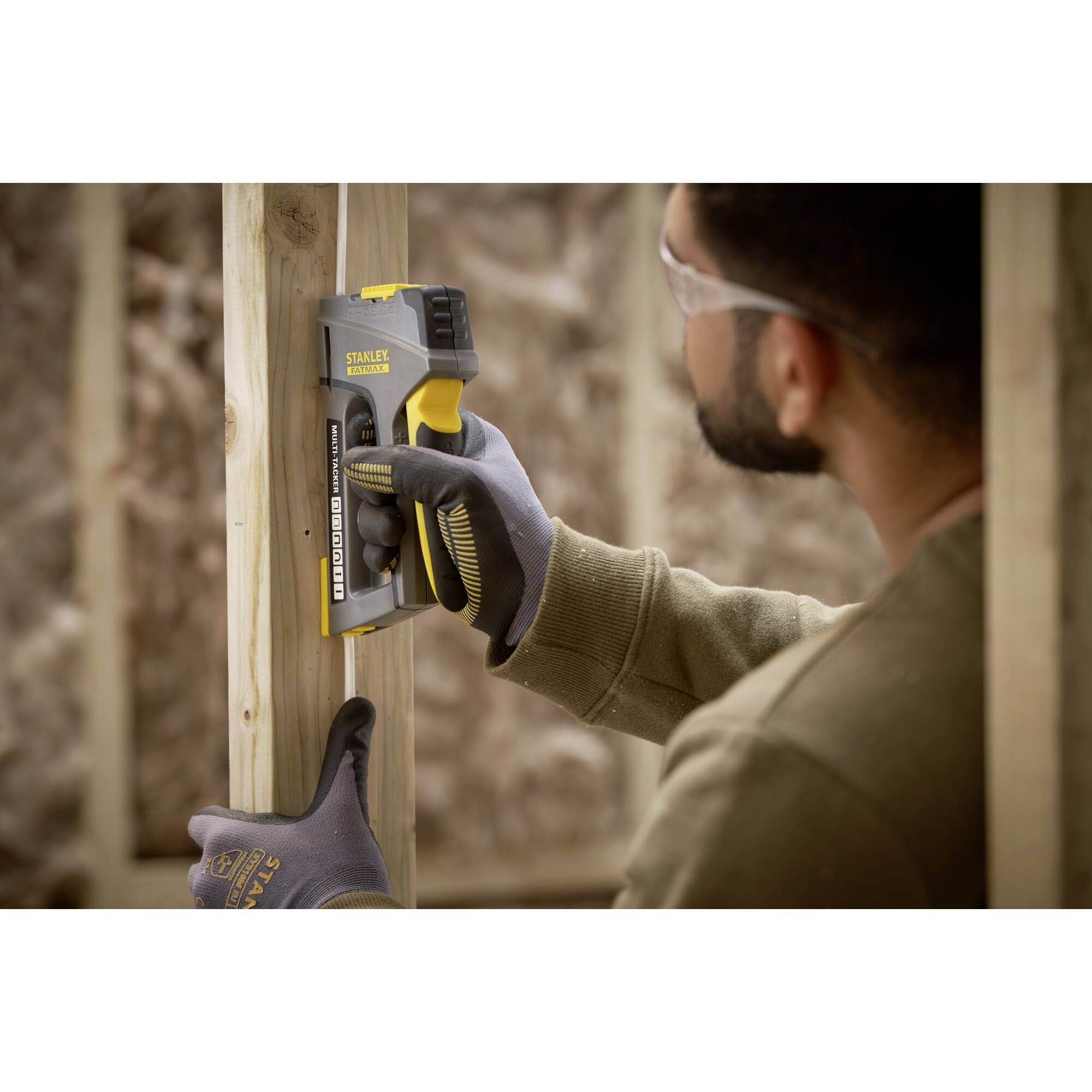 A craftsman is using an electric staple gun to join wooden laths together. He is wearing work gloves and safety glasses.
