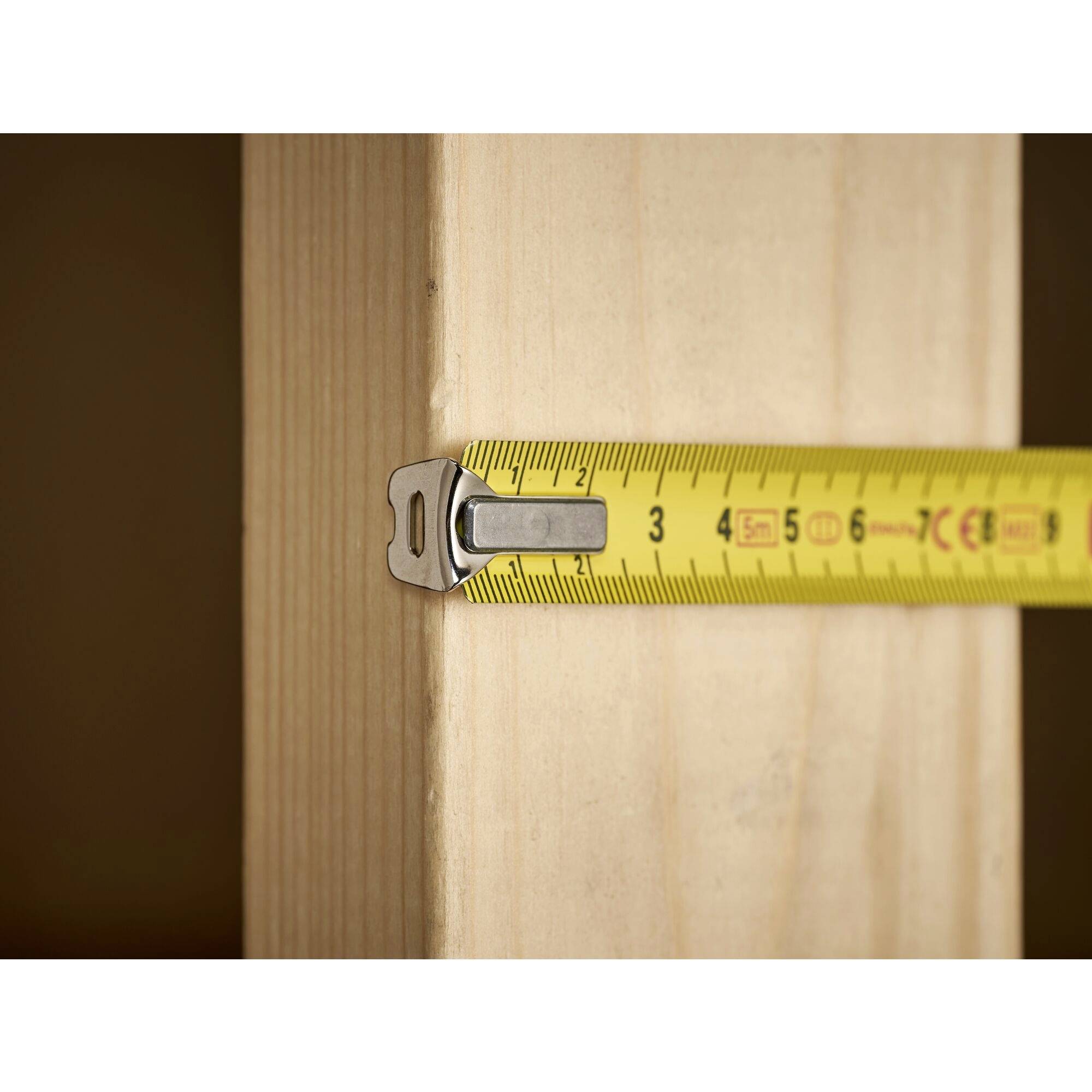 A yellow tape measure is measuring the width of a wooden beam and shows approximately 3 centimetres.