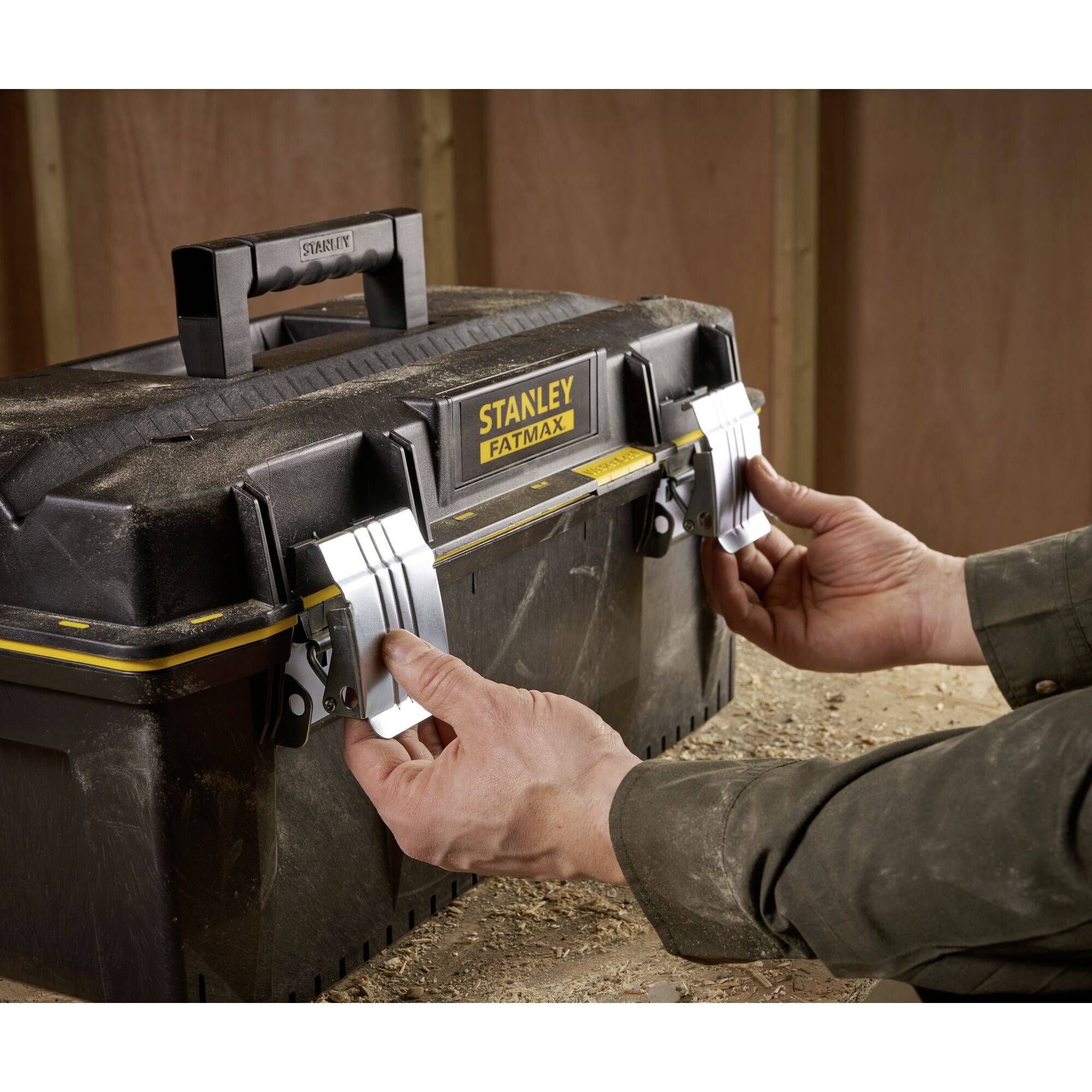 A person opens a 'Stanley Fatmax' toolbox with metal catches in a workshop environment.