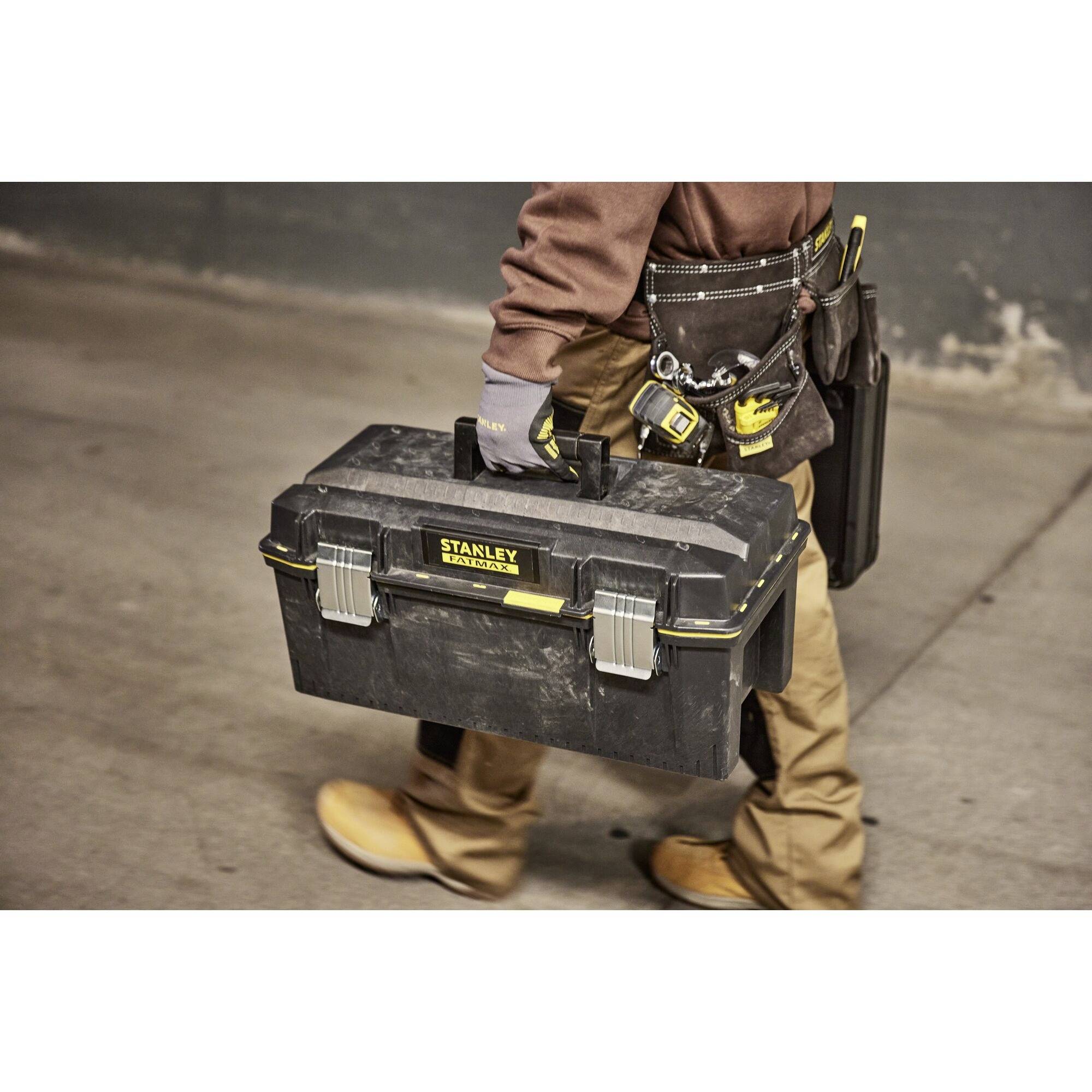 A person is carrying a black toolbox. They are wearing workwear with a belt on which various tools are attached.