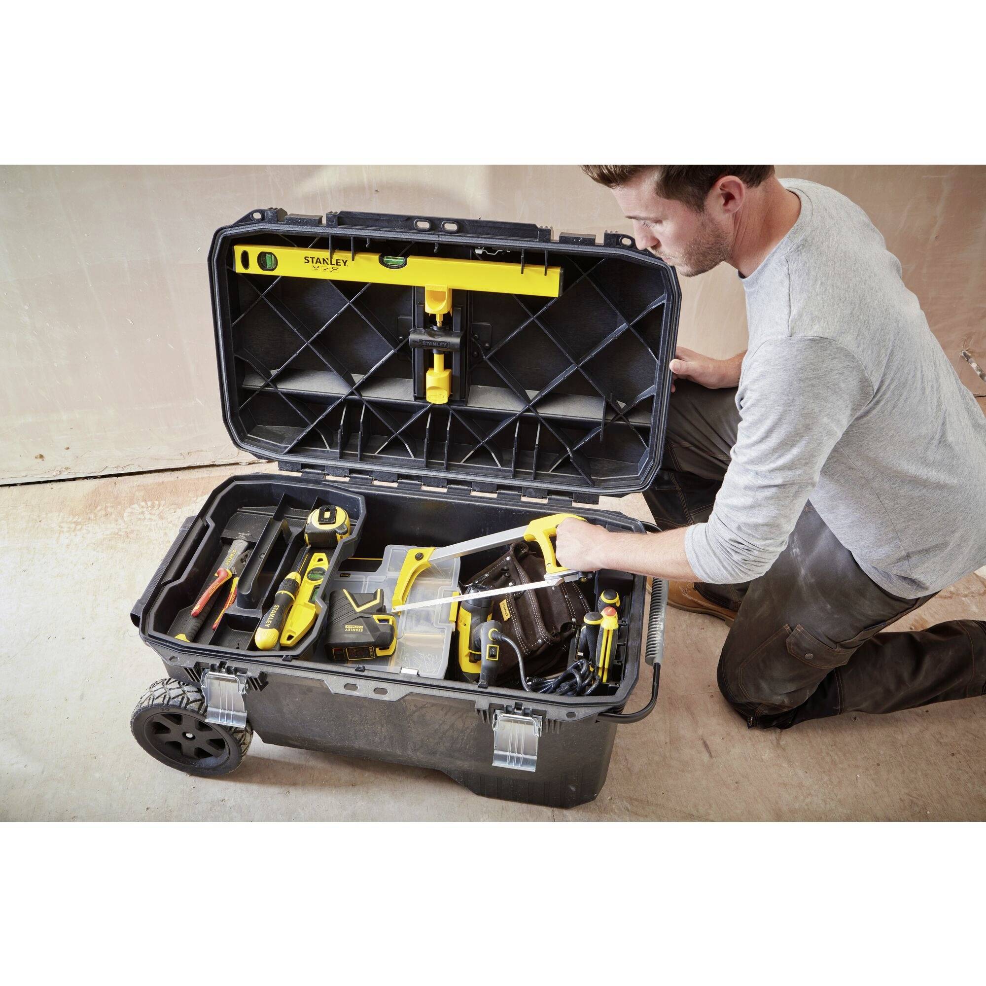 A man is kneeling beside an open toolbox with tools, preparing to work.