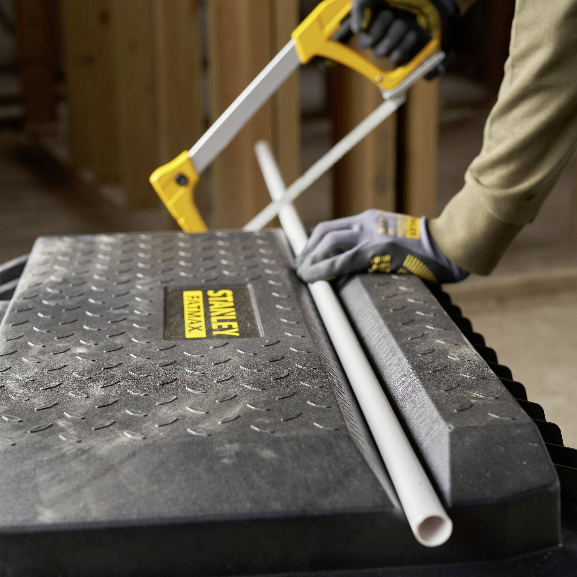 A person is sawing a white PVC pipe with a manual saw on a black, textured stand with a 'Stanley FatMax' inscription.