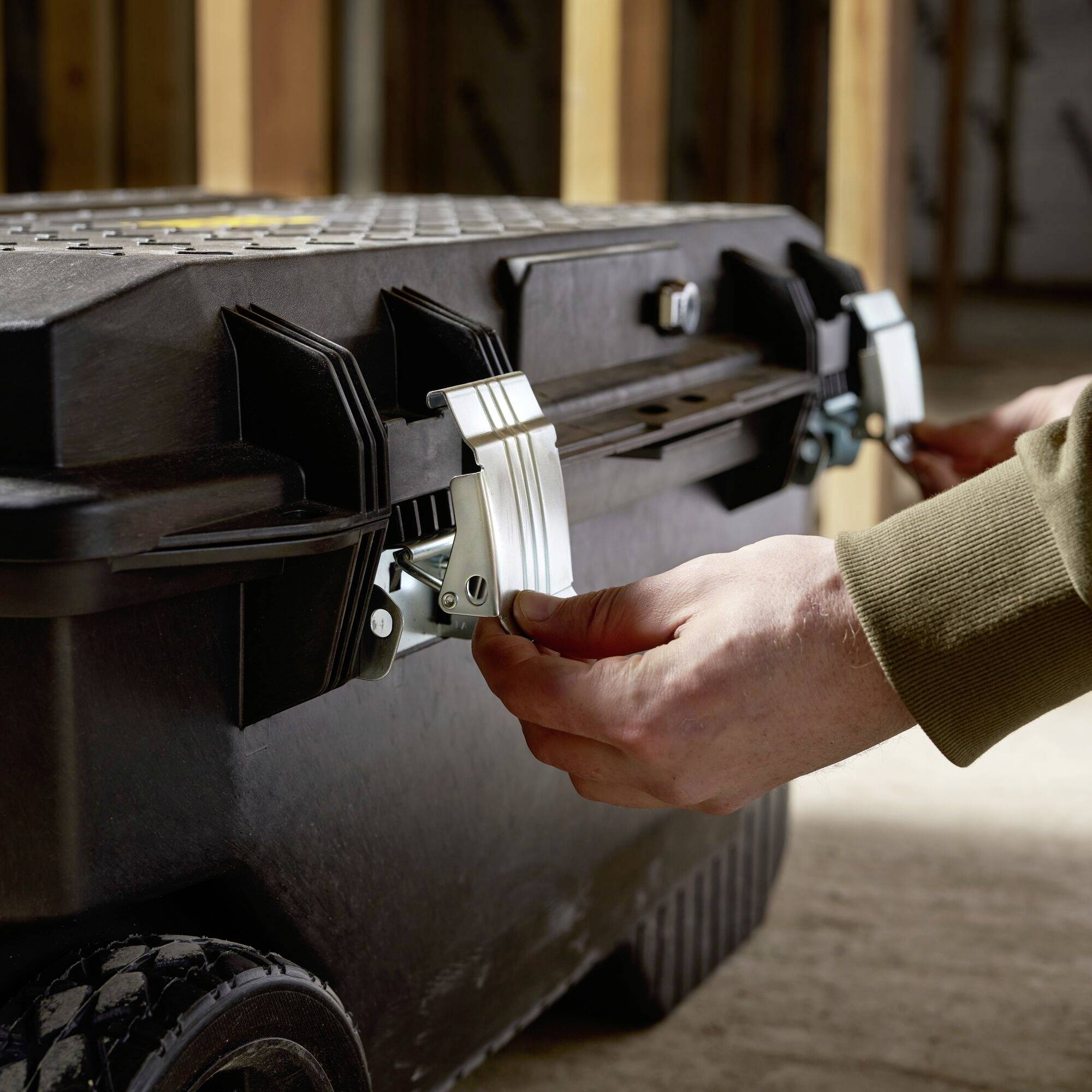 A person closes a large, black toolbox with metal latches in a workshop environment.