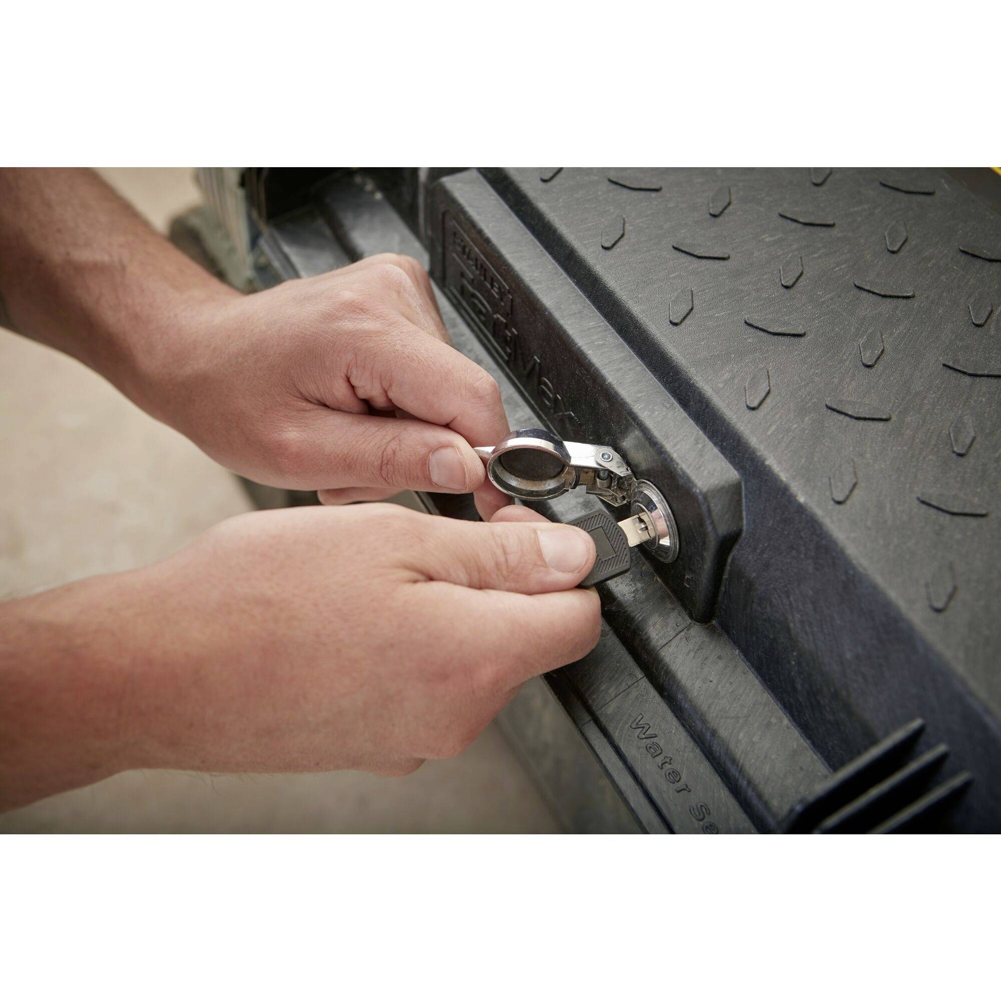 Two hands are turning a small tool in a lock on a textured black surface.