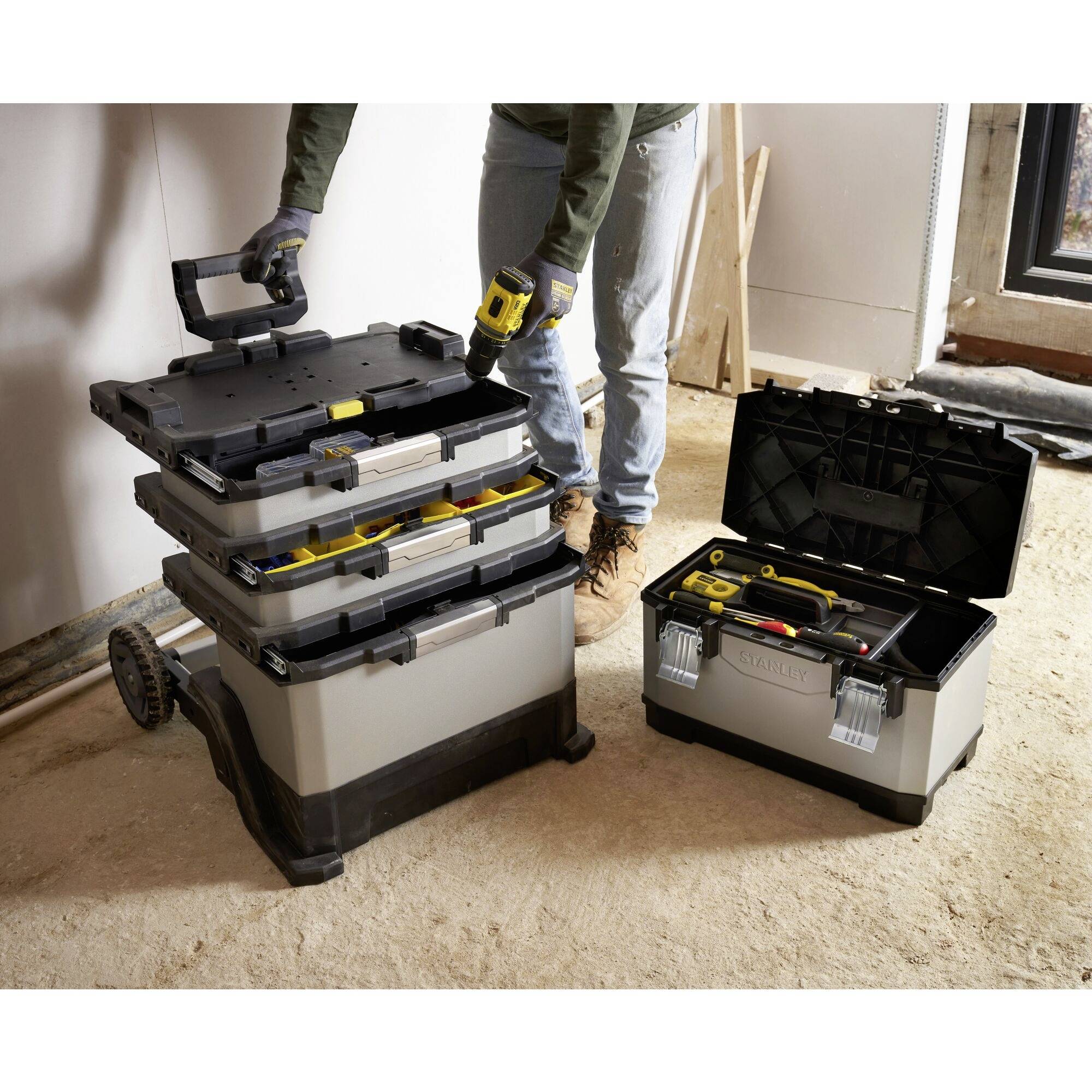 Workstation with a toolbox on the ground; a person wearing gloves is sorting yellow tools and preparing for construction work.