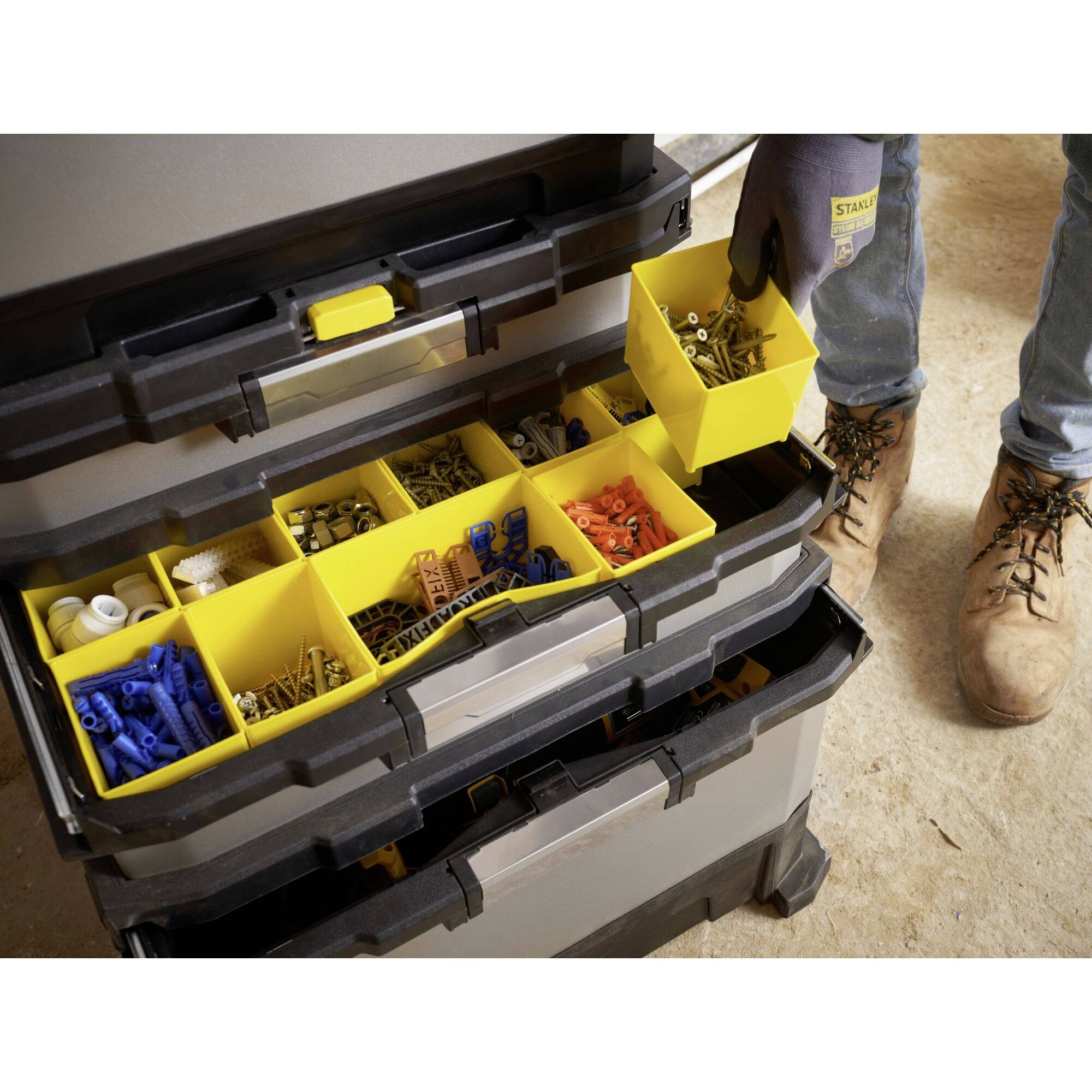 A person removes a yellow container full of screws from an open toolbox with multiple compartments filled with small parts.
