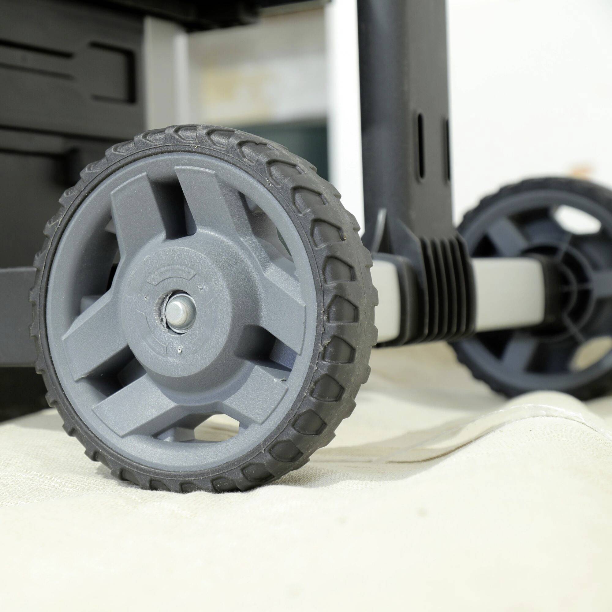 Close-up of a large, grey plastic wheel of a transport trolley on a light floor. Another wheel is visible in the background.