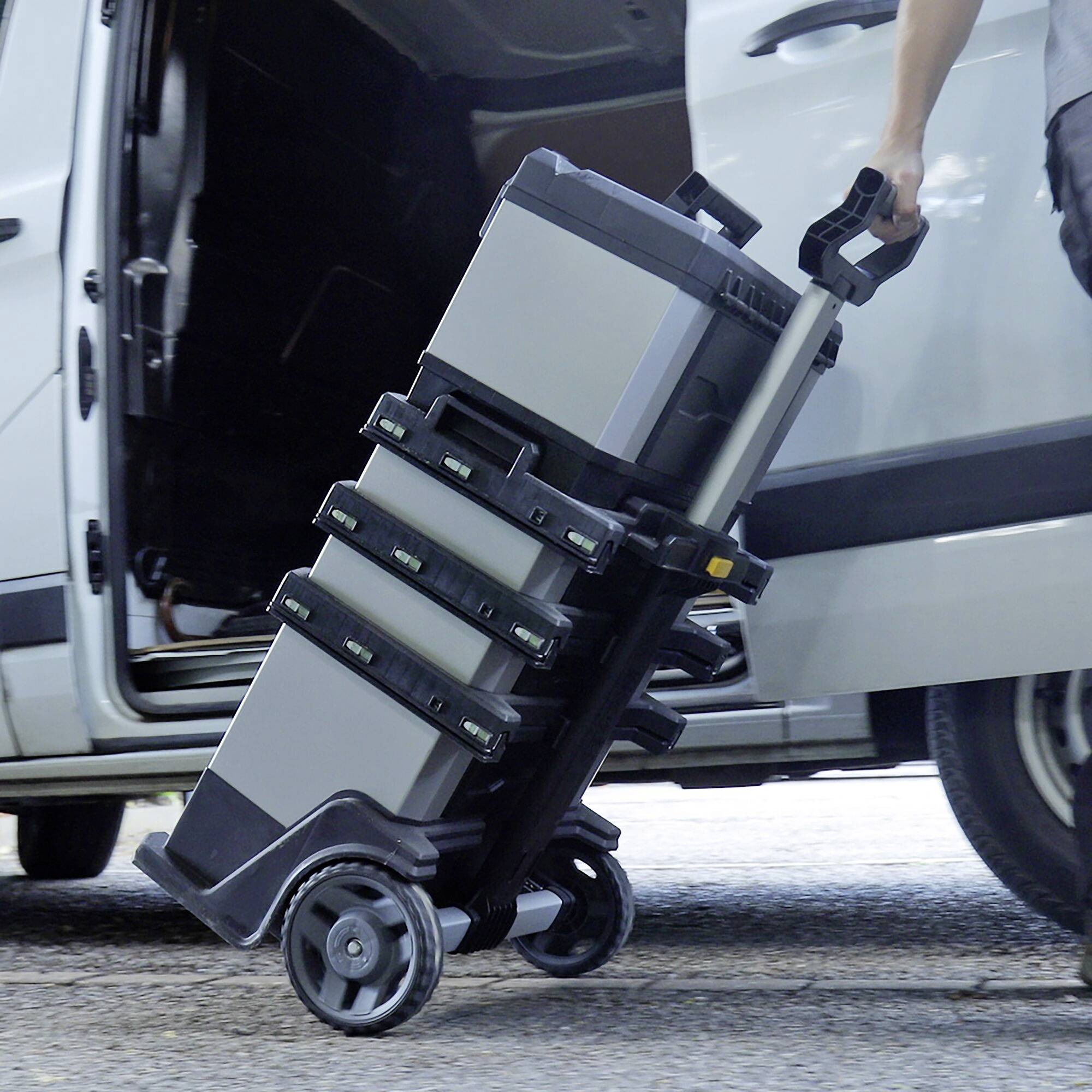 A person is pushing a trolley with stacked toolboxes out of a vehicle.