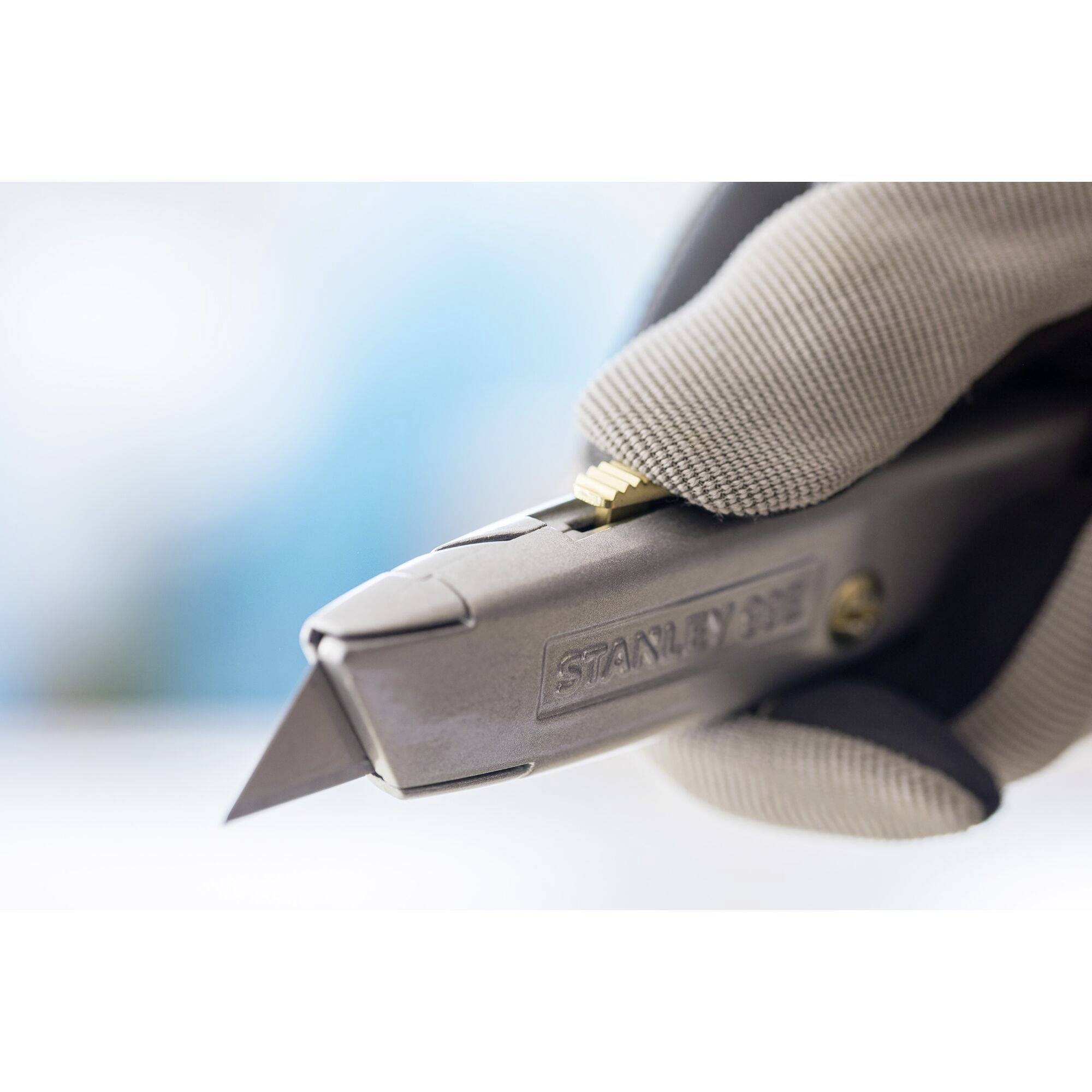 'Close-up of a carpet knife held by a gloved hand, ready to cut. Focus is on the blade.'