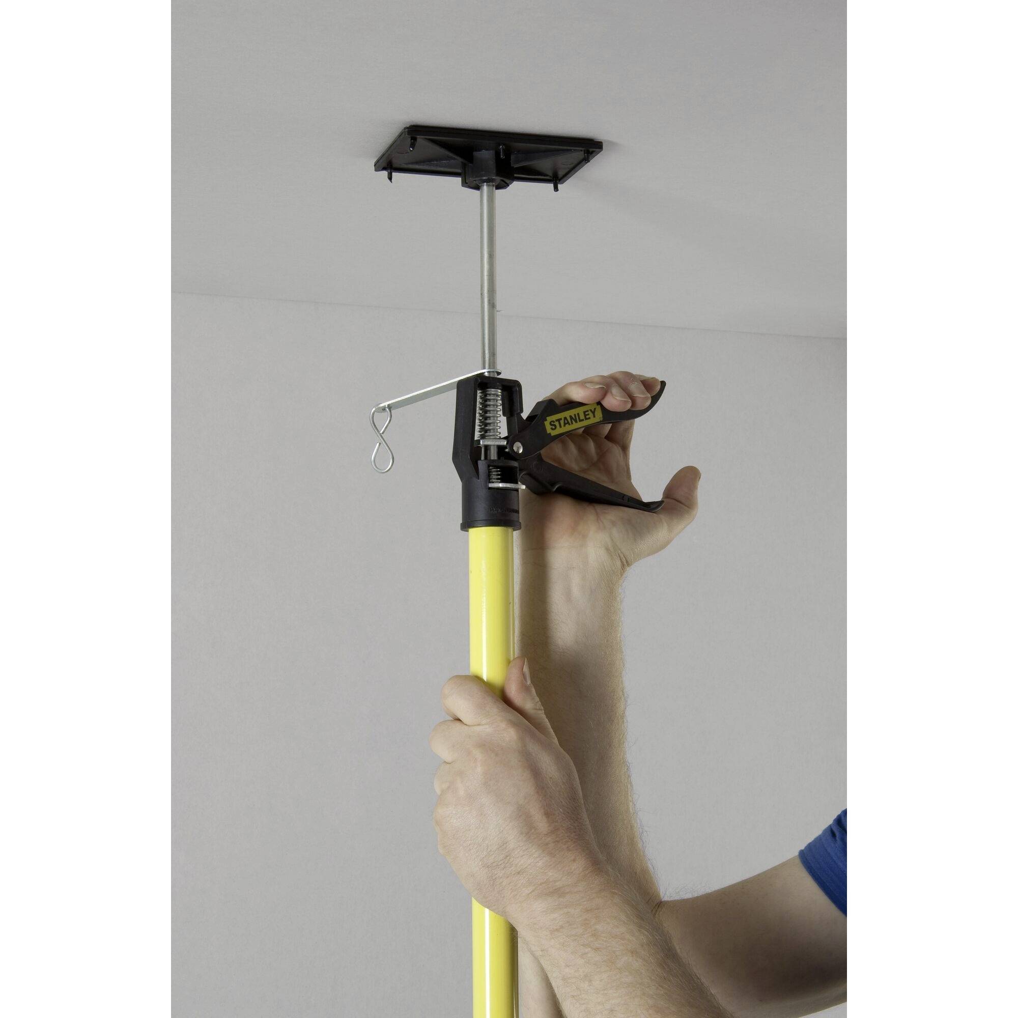 A person is using a yellow pole to secure a rectangular device to the ceiling.