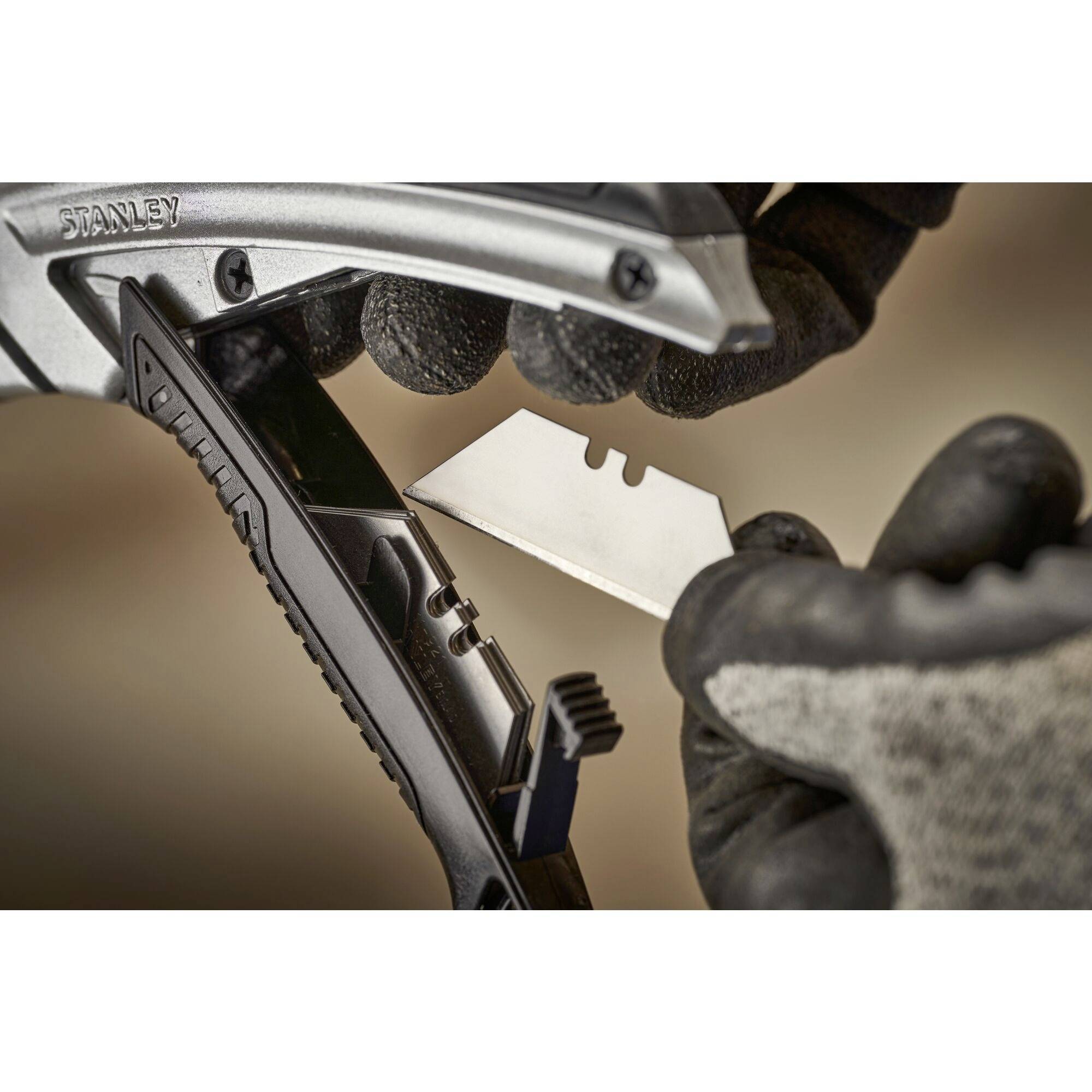 A person wearing black gloves is changing a blade in a utility knife. The blade is straight and silver.