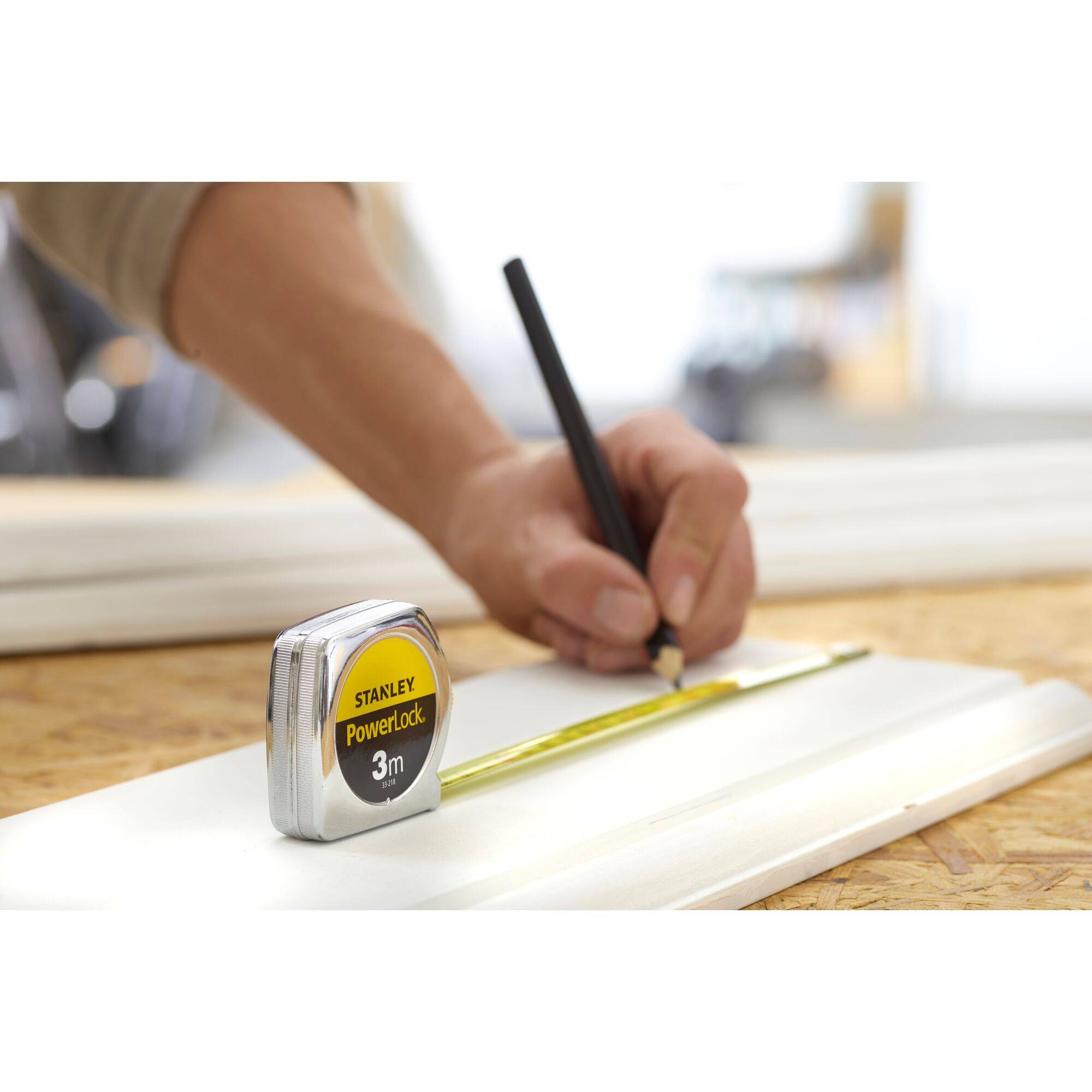 'A person is drawing a line on a piece of wood with a pencil, while a 3m measuring tape holds down the short end.'