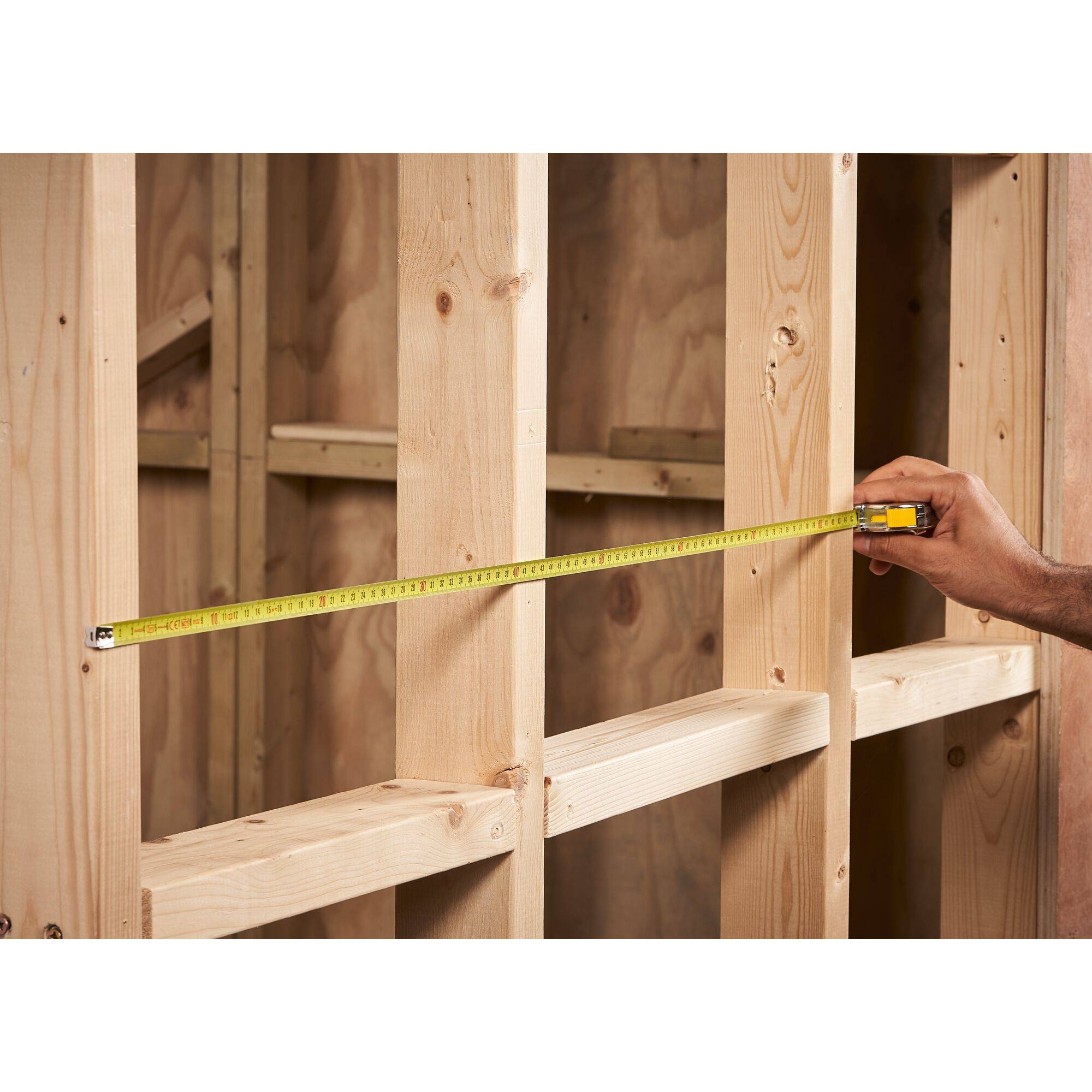 A measuring tape is held by a hand measuring the distance between wooden frames in a building under construction.