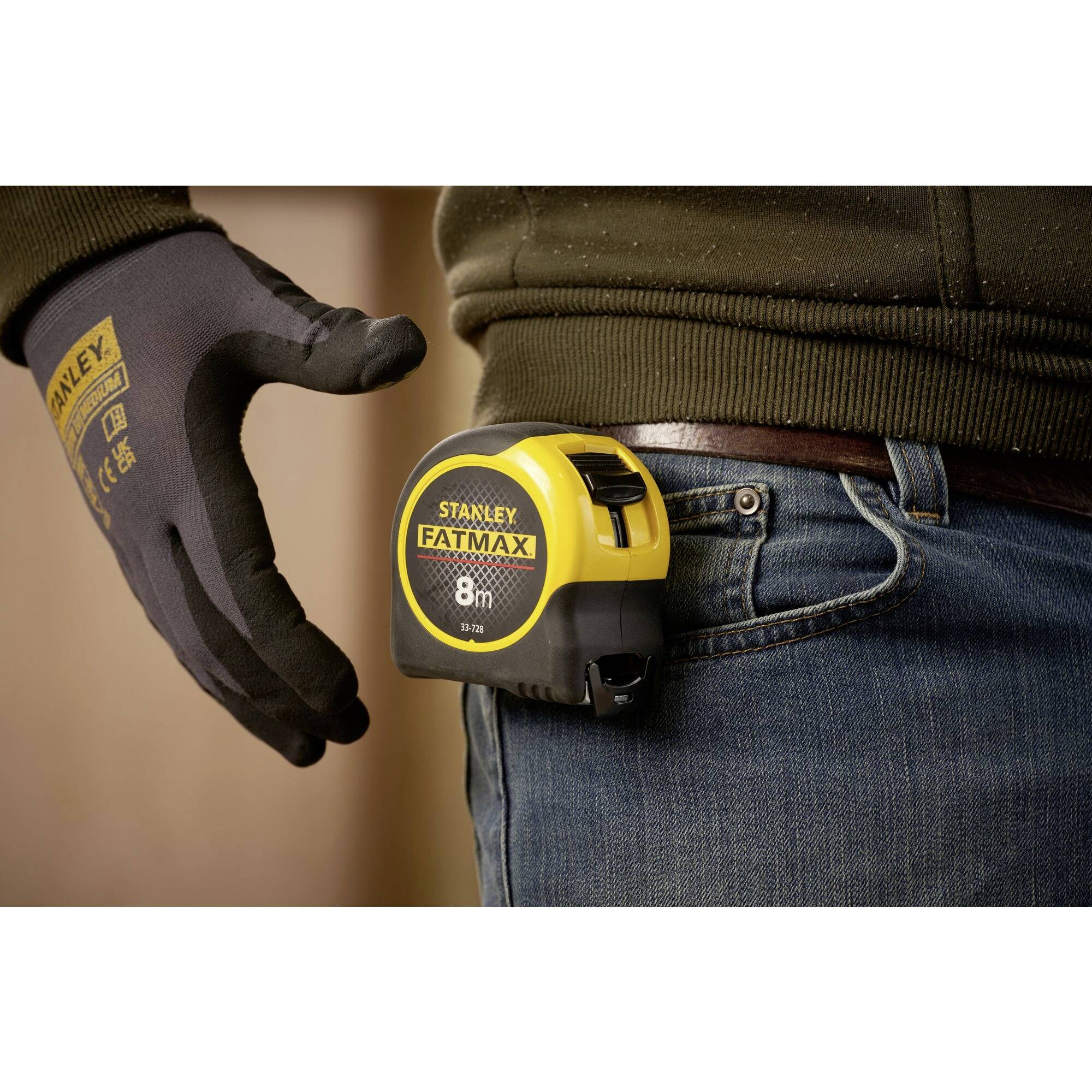 A person is wearing a 'Stanley Fatmax' tape measure on their trouser belt, while wearing a black glove.