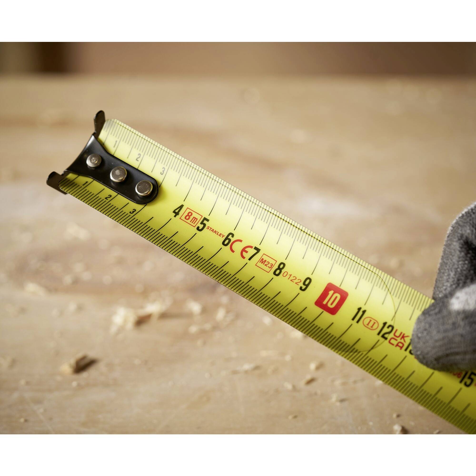 A tape measure on a wooden table, showing a length of 10 centimetres. A hand is holding the tape in place.