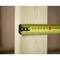 A yellow tape measure is measuring the width of a vertical wooden board. The tape shows approximately 6 centimetres.