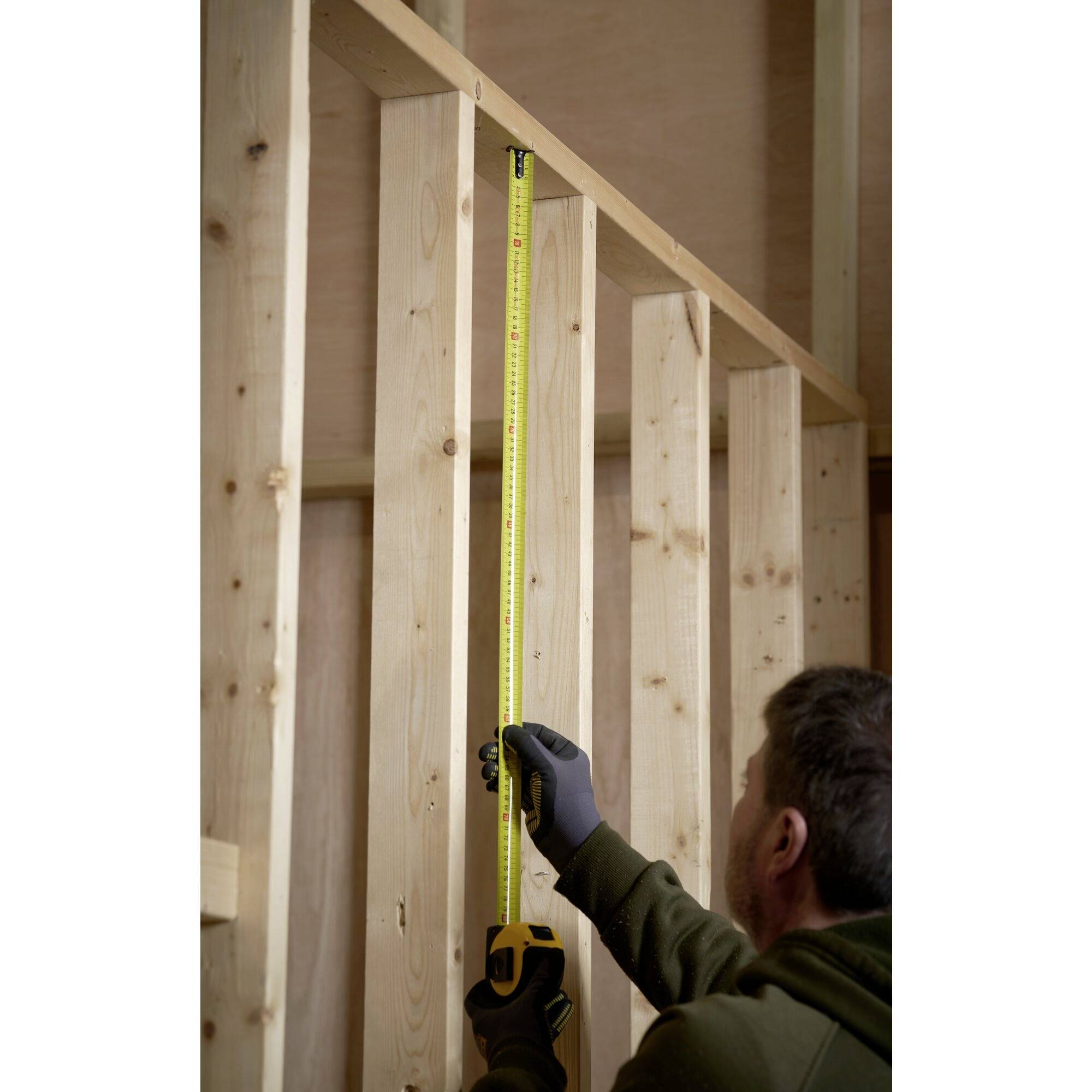 A person is measuring the height of a wooden frame in a room, possibly as part of a construction or renovation project.