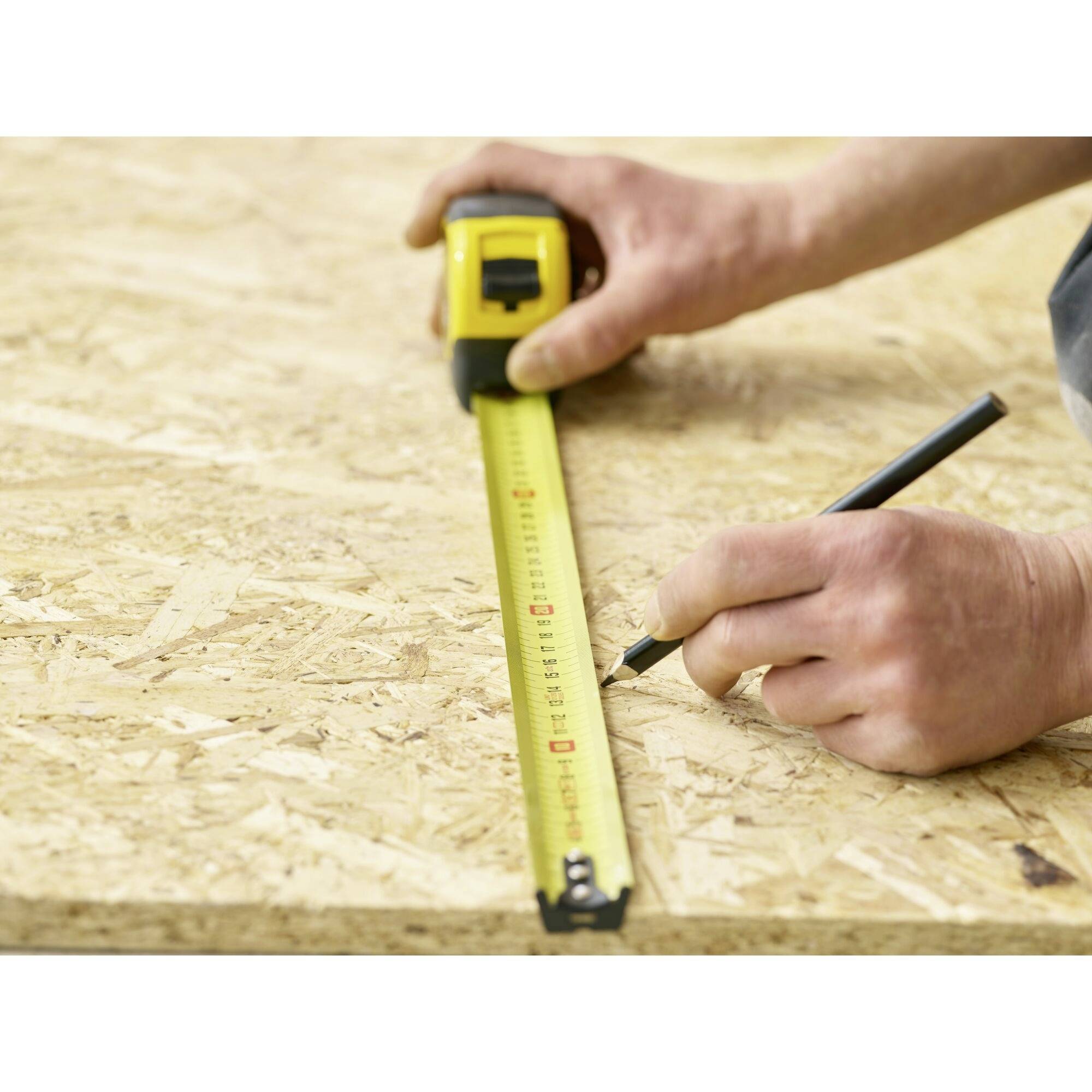 A hand holds a tape measure on a wooden board; another hand is drawing a mark at 50 cm.