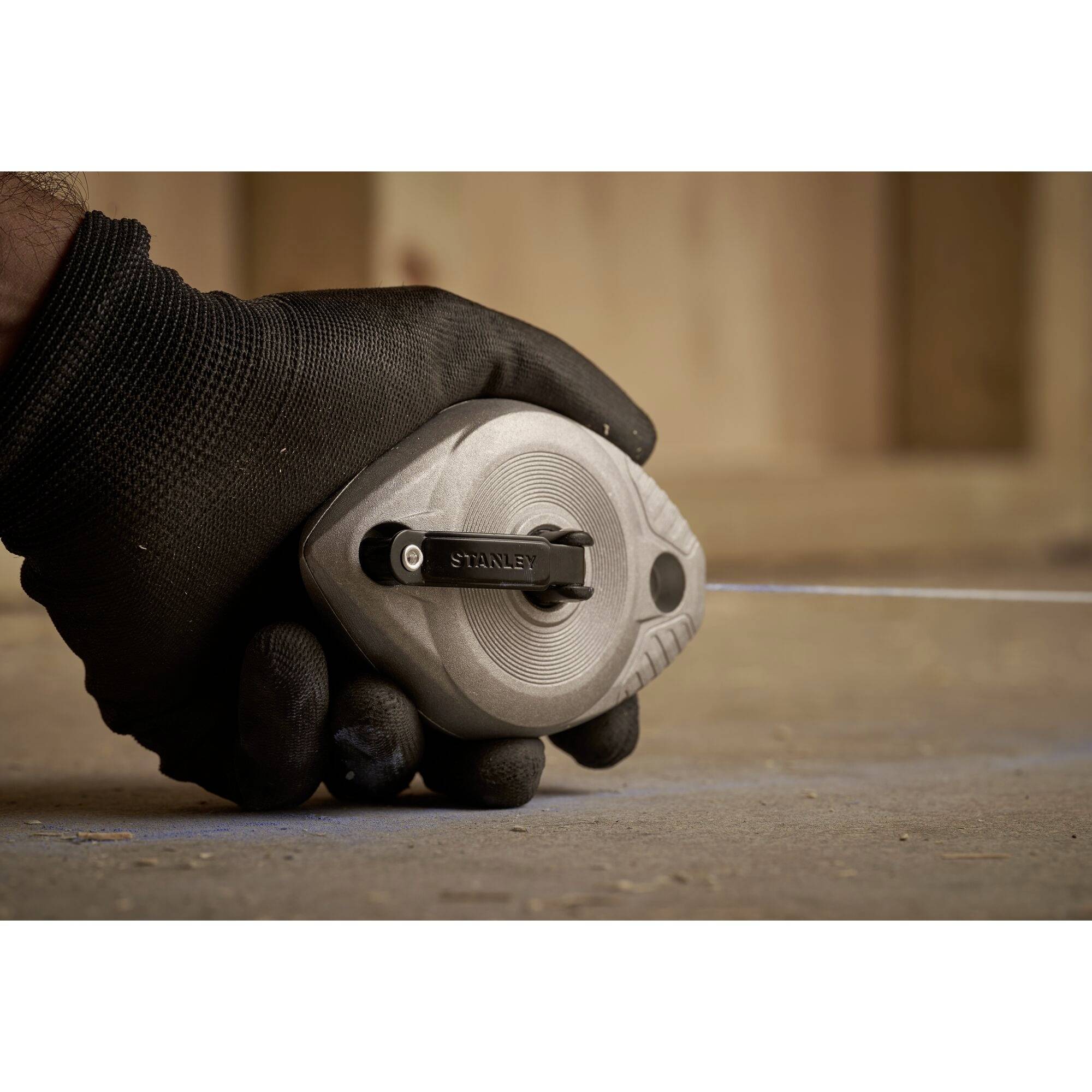 A gloved hand holds a measuring tape on the ground, which is used for precise measurements during construction.