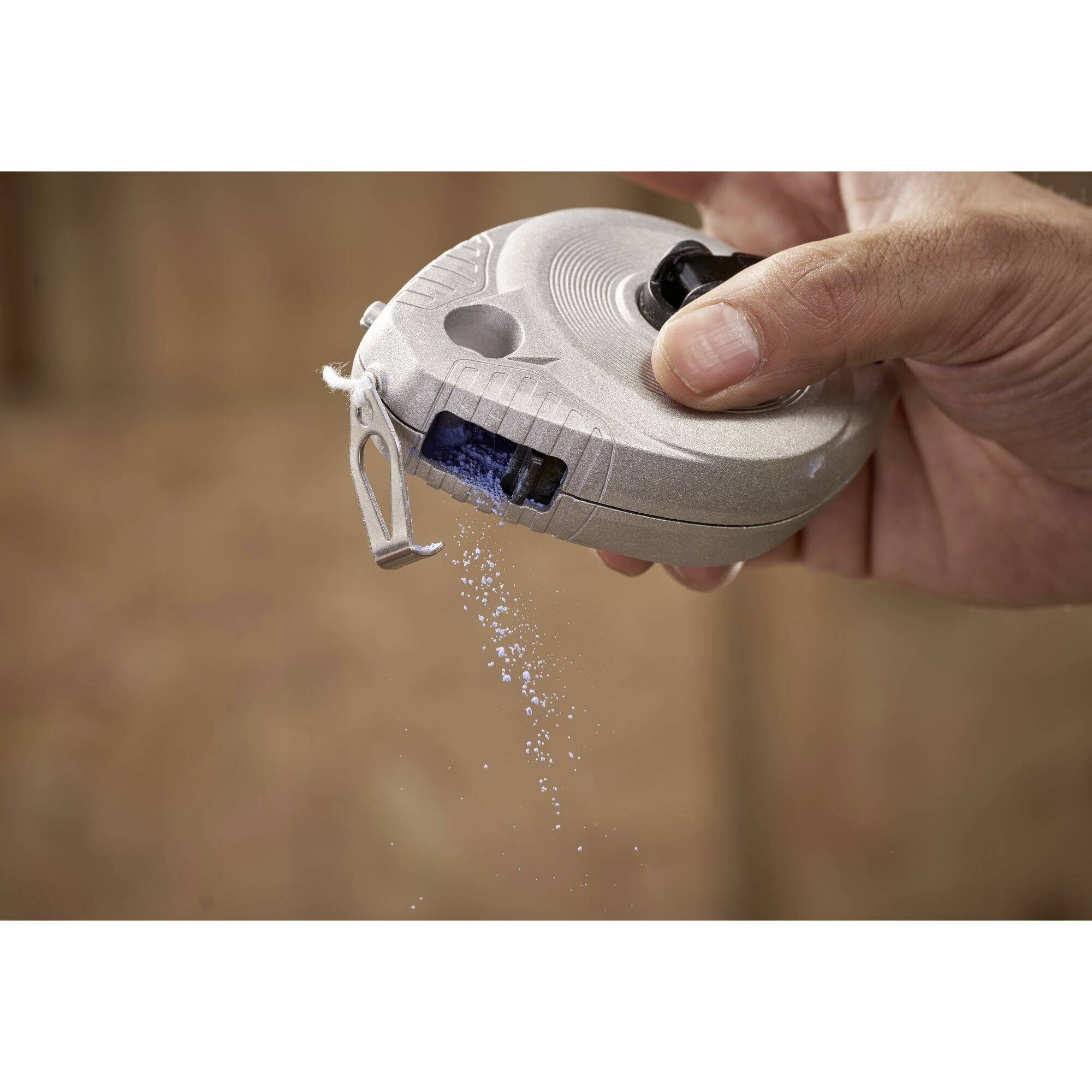 A hand presses a chalk line, with blue chalk powder streaming out. The tool is used for marking straight lines.