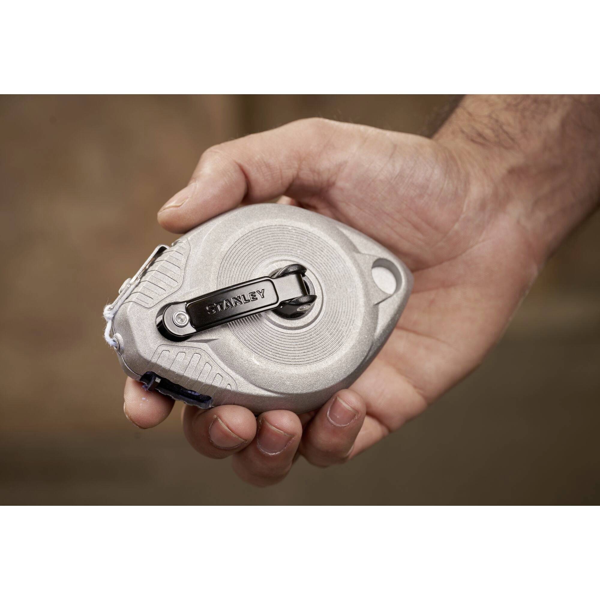 A hand is holding a grey tape measure in a closed position.