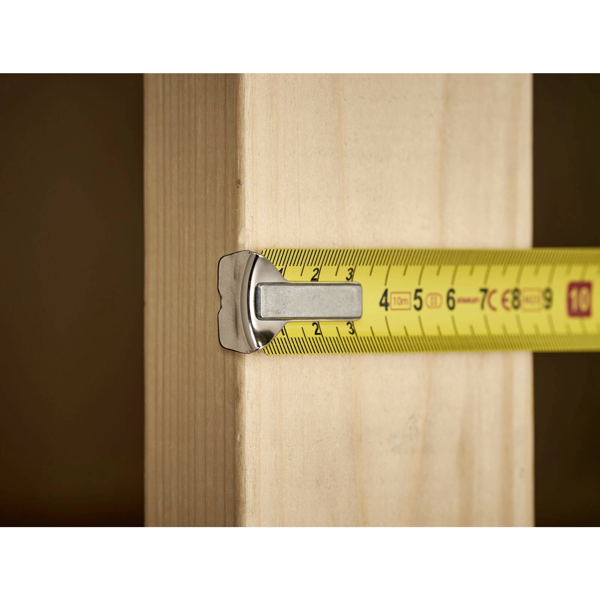 A yellow tape measure is measuring the width of a wooden board and shows almost 9 centimetres.