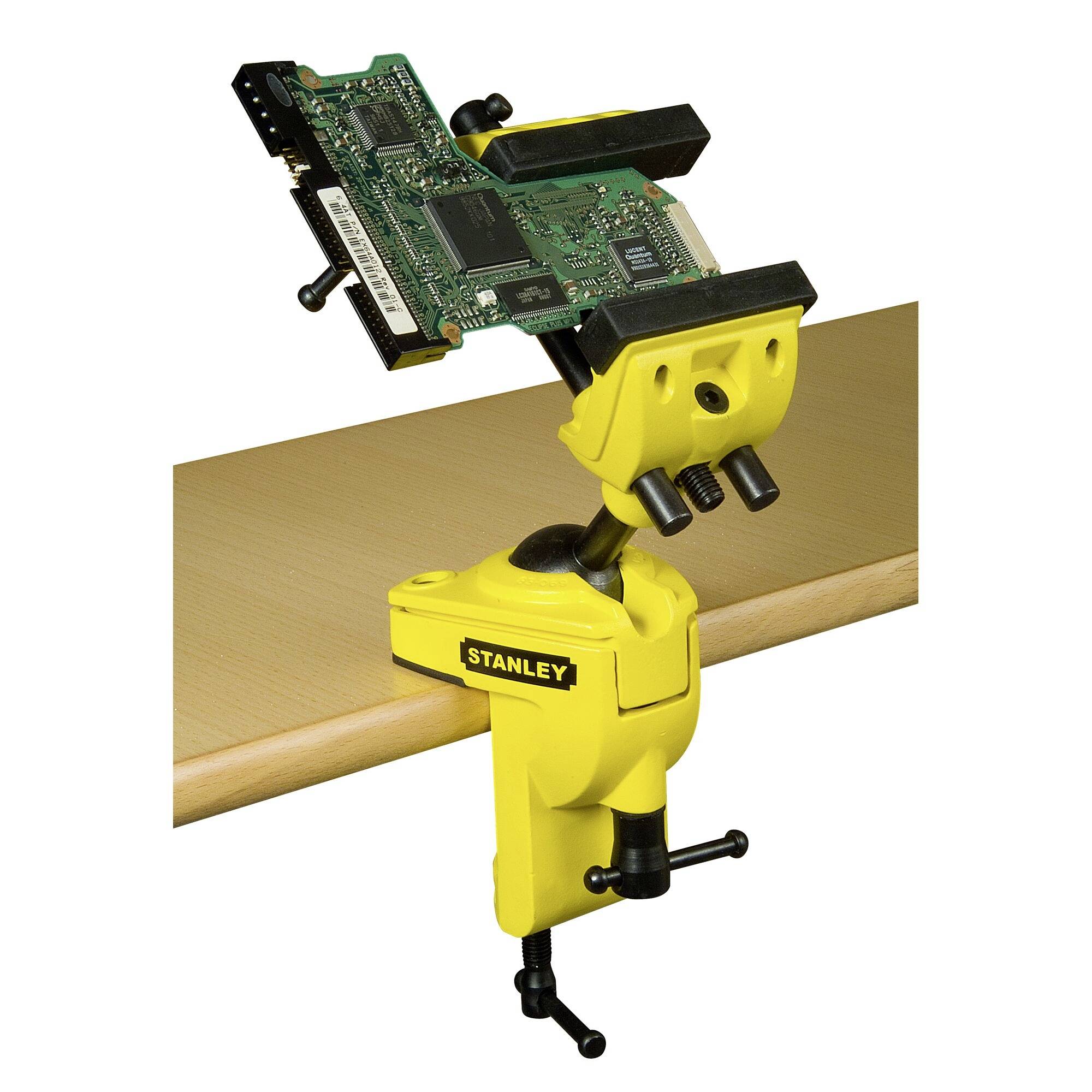 'A yellow Stanley bench clamp holds an electronic circuit board over a table edge, showing detailed work or a repair process.'