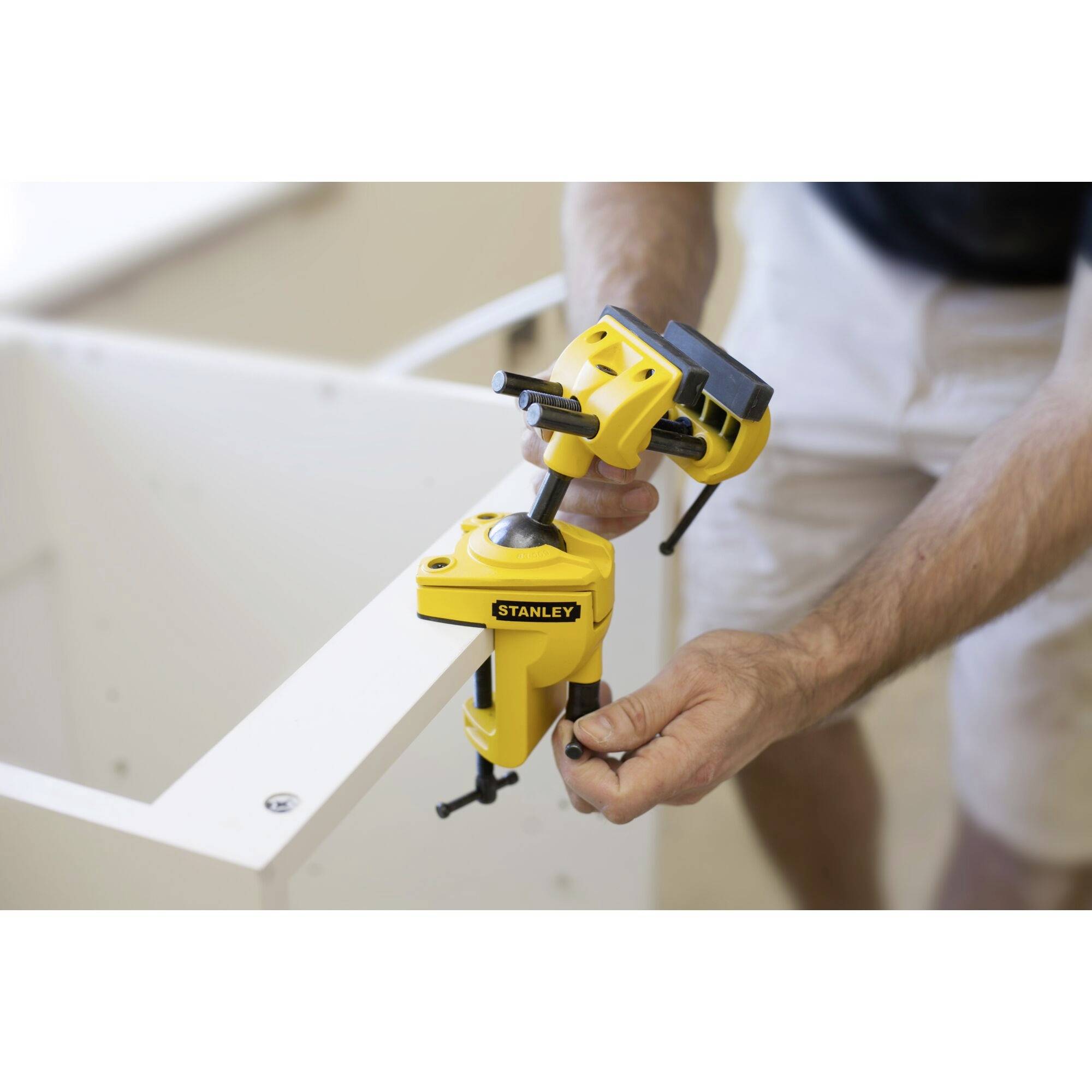 A person is securing a piece of furniture with yellow clamps. The clamps bear the brand name 'Stanley'.